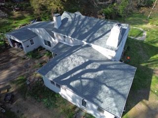 Aerial view of a gray-roofed house surrounded by trees and green yard.