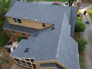 Aerial view of a tan house with a gray shingled roof and driveway beside it.