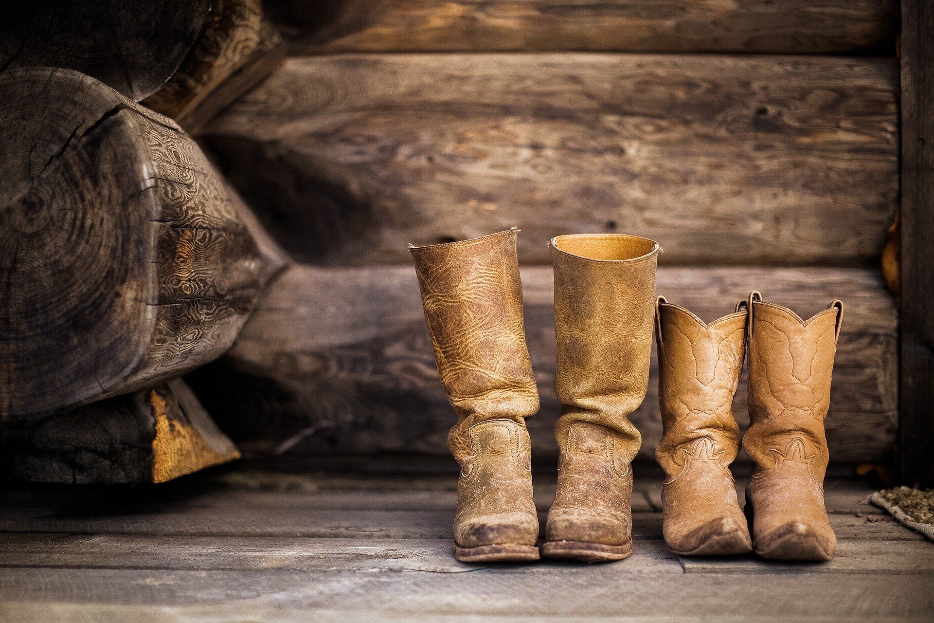 Pair of leather boots on a wooden surface in front of a log cabin wall.