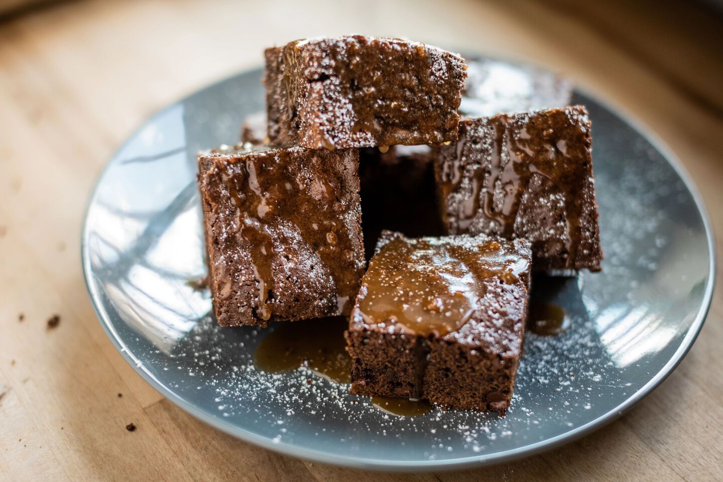 Brownie squares with sauce on a blue plate, dusted with powdered sugar, on a wooden surface.