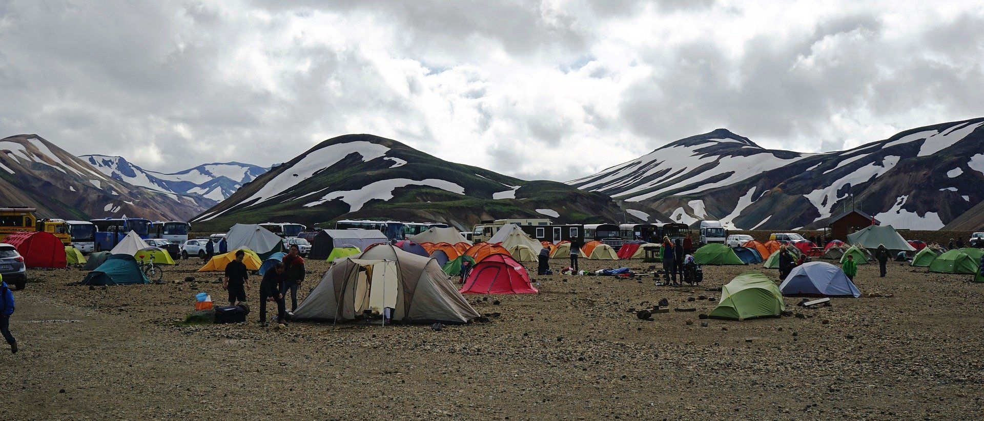 Camping tents on a gravel surface with snowy mountains in the background under a cloudy sky.