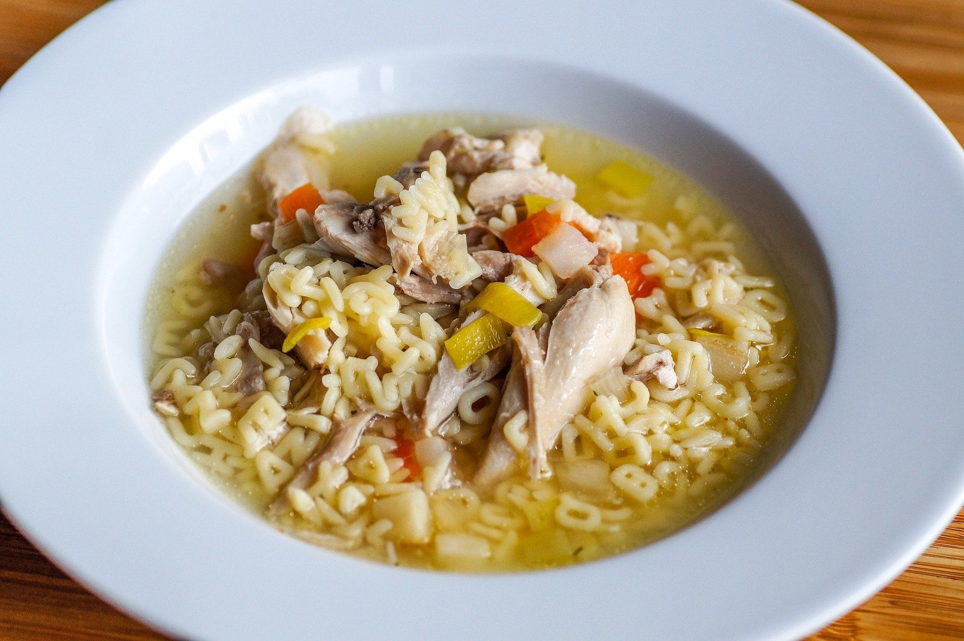 Chicken noodle soup in a white bowl, with shredded chicken, yellow noodles, and diced vegetables.