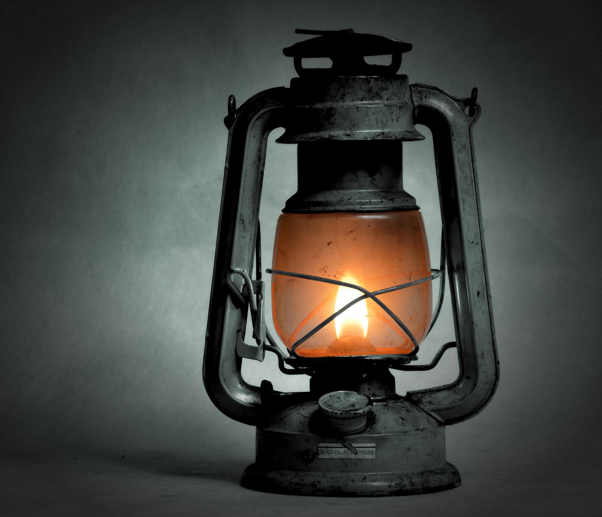 Lit antique lantern, orange glow, metal frame, dimly lit setting.