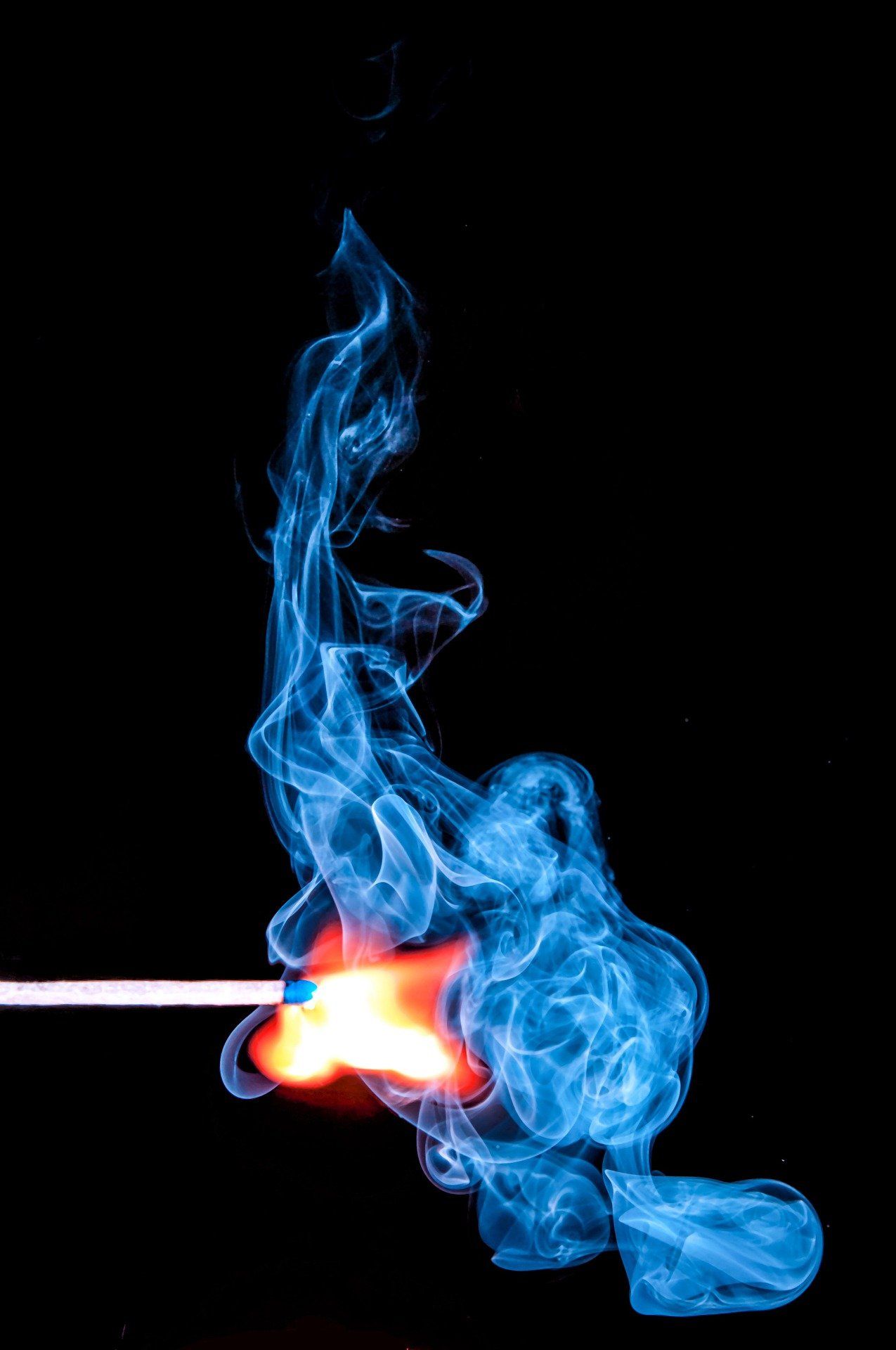 A match head ignites, emitting orange flame and blue smoke against a black background.