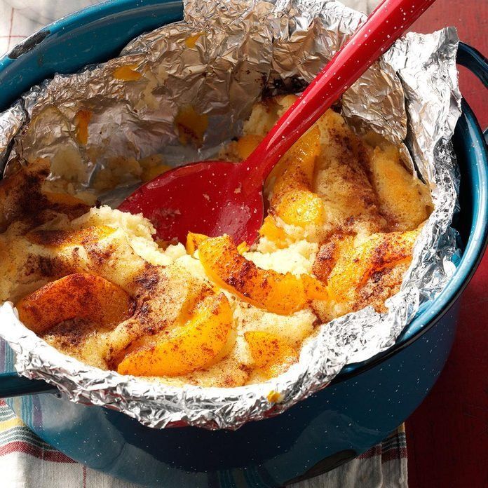 Cobbler with peaches, cooked in a blue pot with a red spoon.