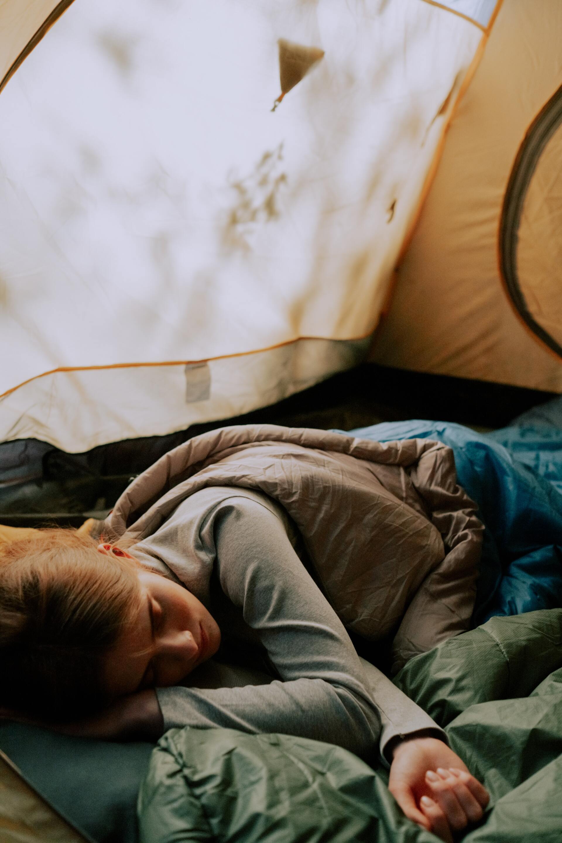 Person sleeping inside a tent on a sleeping bag, tent flaps open.