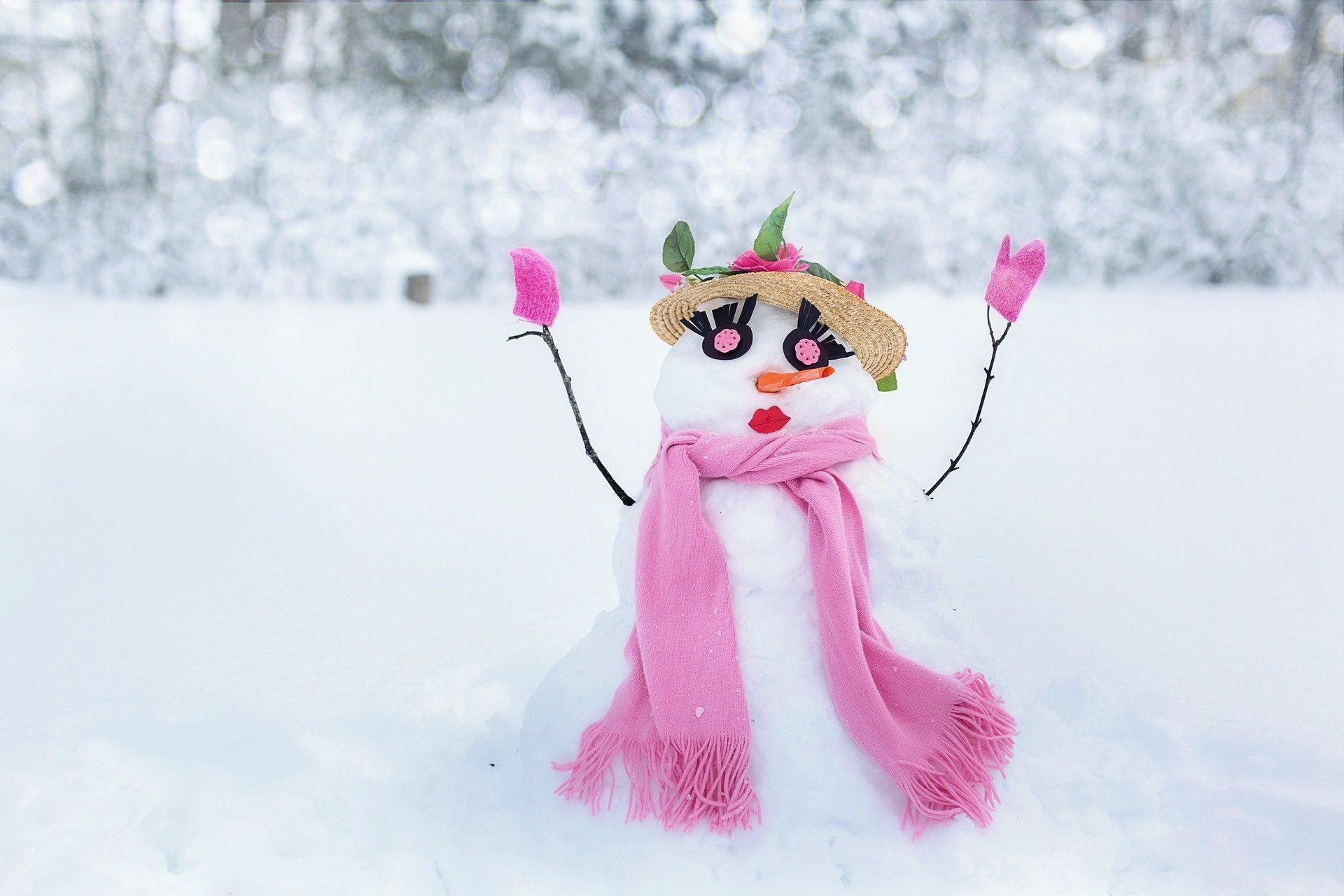 Snowman with pink scarf, gloves, and a decorative face in snowy setting.