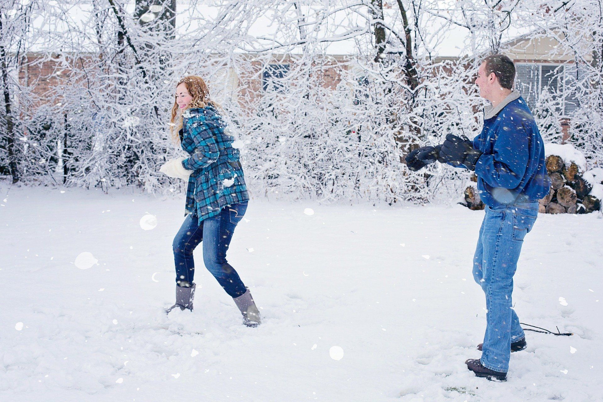 Couple in a snowy backyard, playfully throwing snowballs at each other.