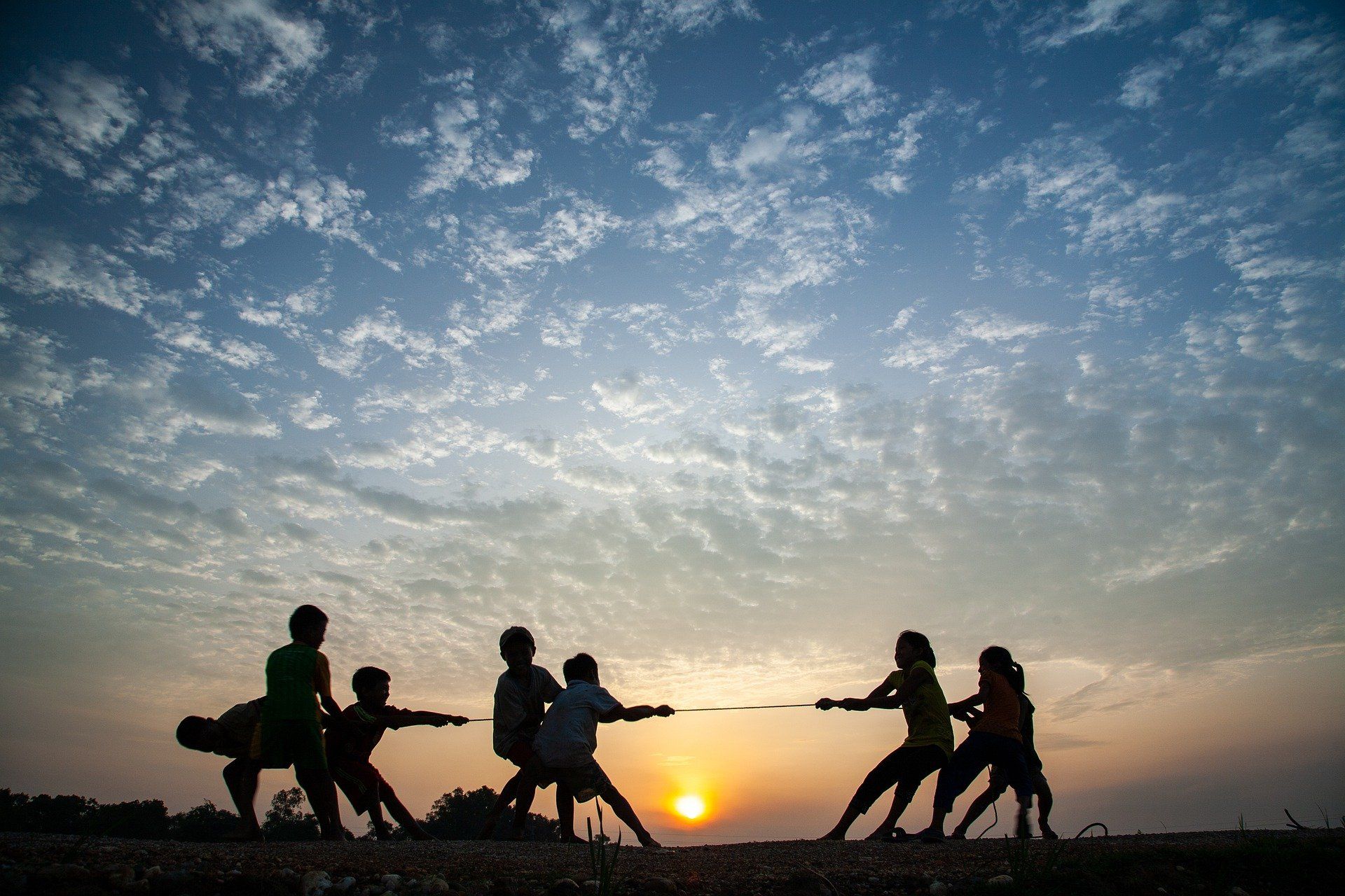 Silhouette of children playing tug-of-war against a sunset sky.