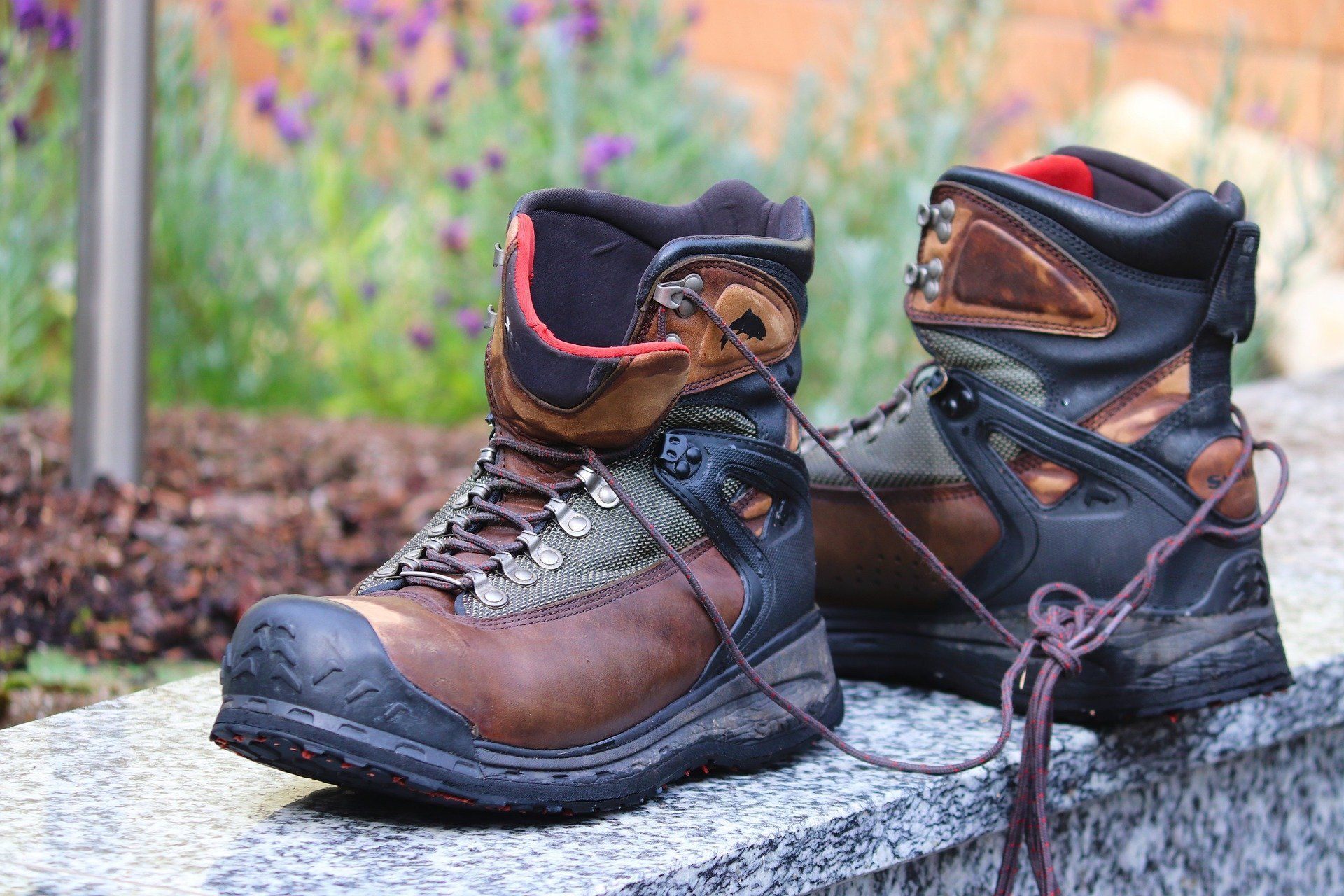 Pair of brown and black hiking boots with laces resting on a stone surface outdoors.
