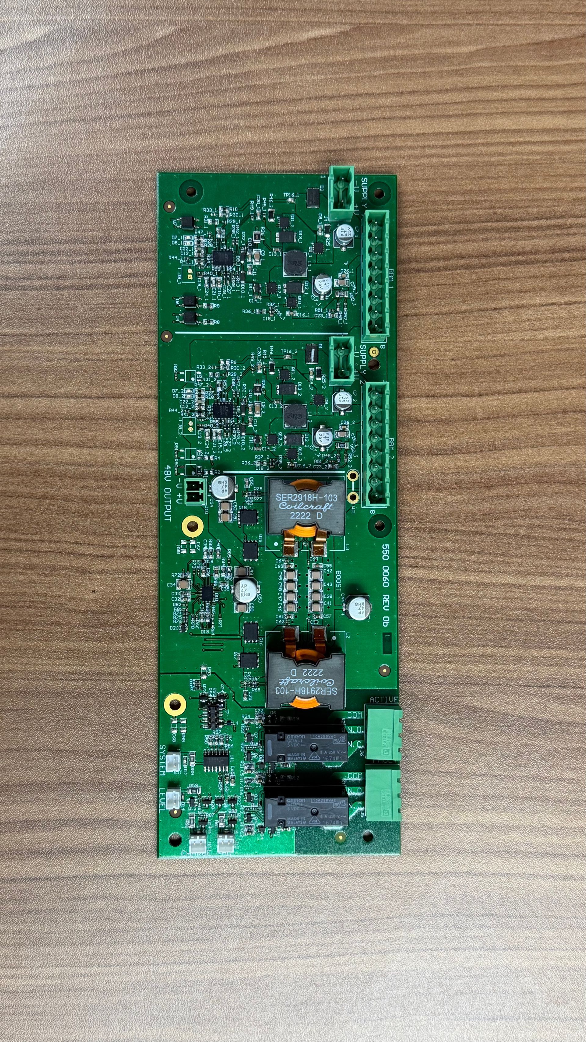 A green rectangular circuit board with various electronic components, connectors, and inductors placed on a wood surface.
