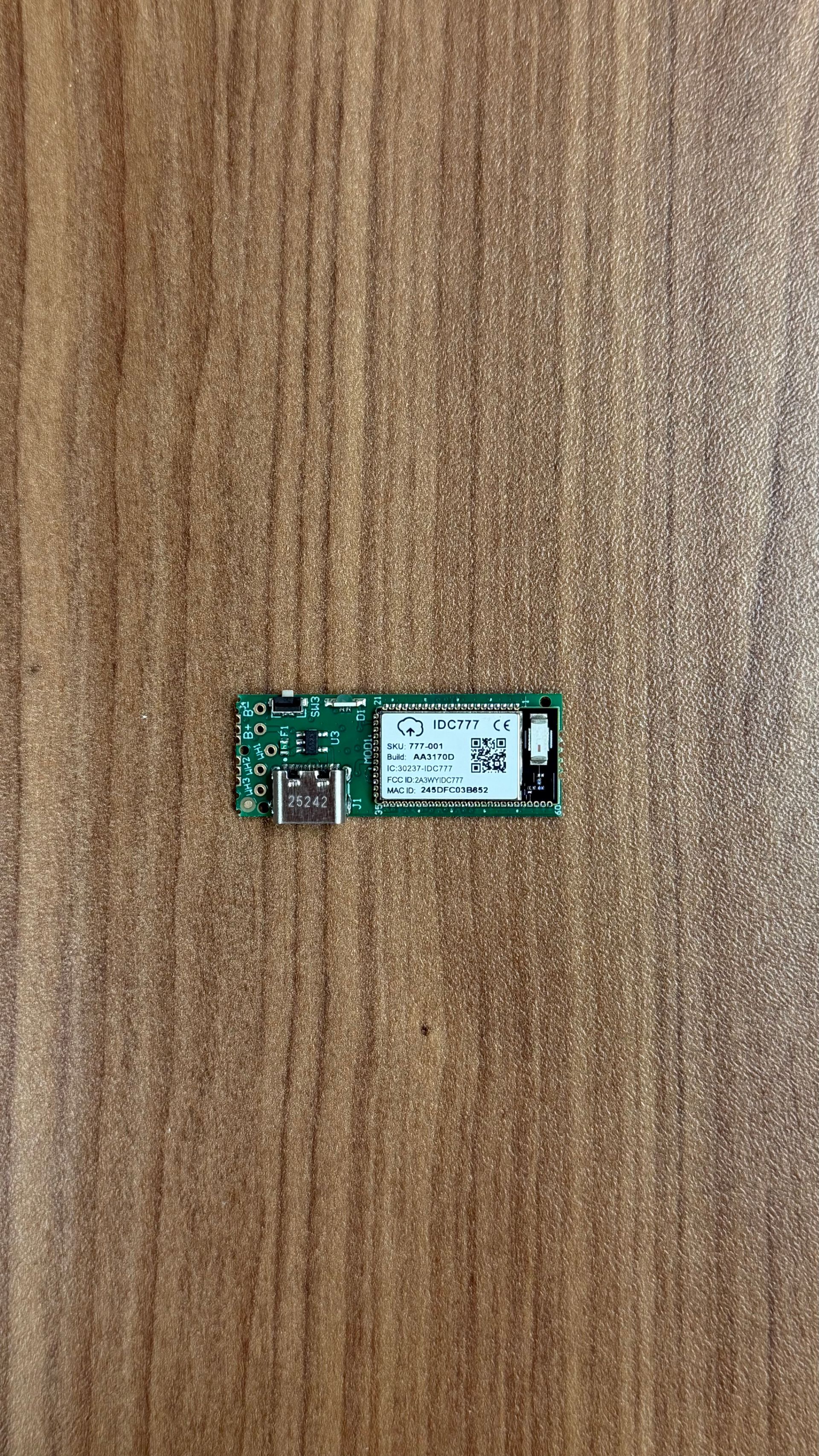 A green circuit board featuring a USB-C port and a small white wireless module, centered on a brown wood-grain surface.