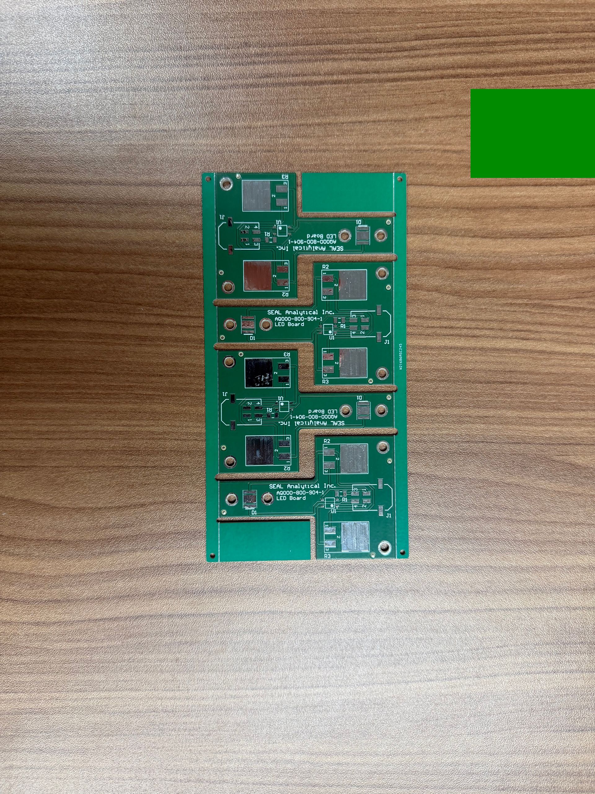 A rectangular green circuit board panel on a wooden surface with several individual component sections attached.