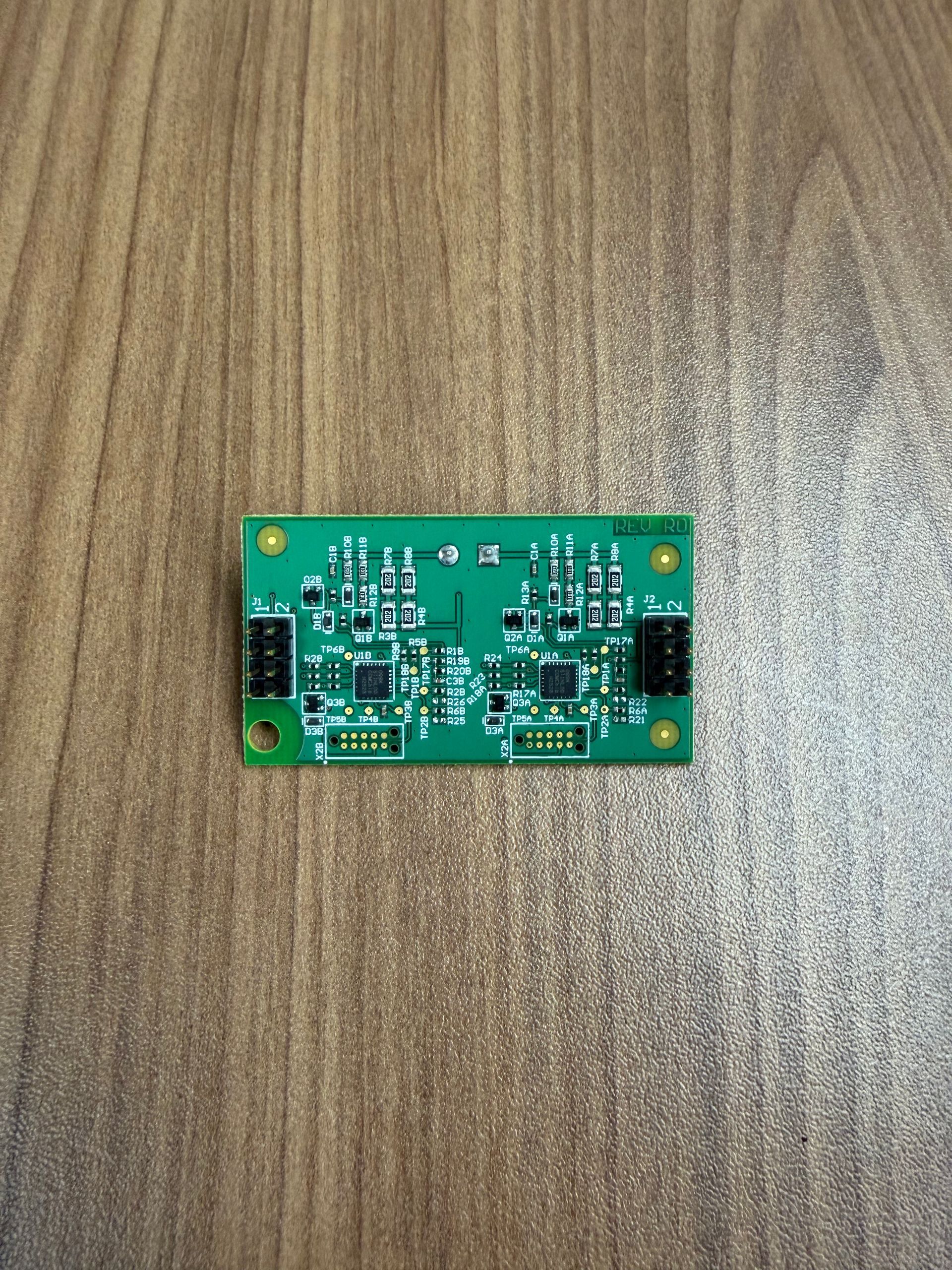 A green rectangular circuit board with two 4-pin connectors and electronic components, lying on a wooden surface.