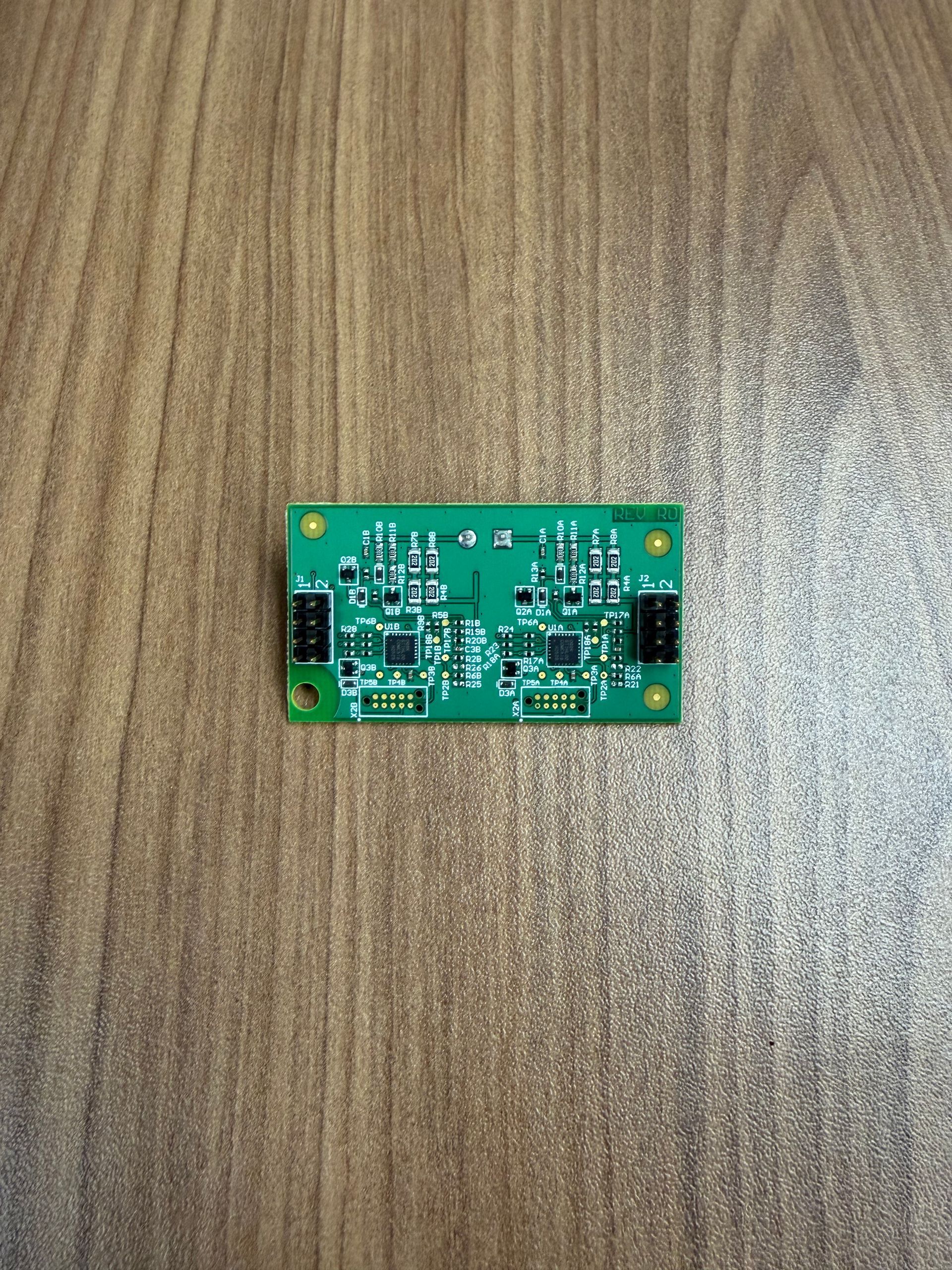 A small green circuit board with two integrated chips and connectors, positioned centrally on a wood-grain surface.
