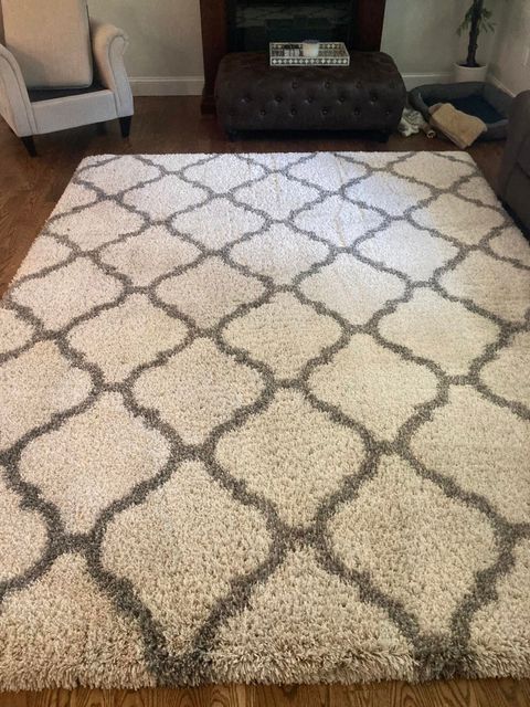 Living room with a cream patterned rug, gray chair, dark ottoman, and hardwood floor.