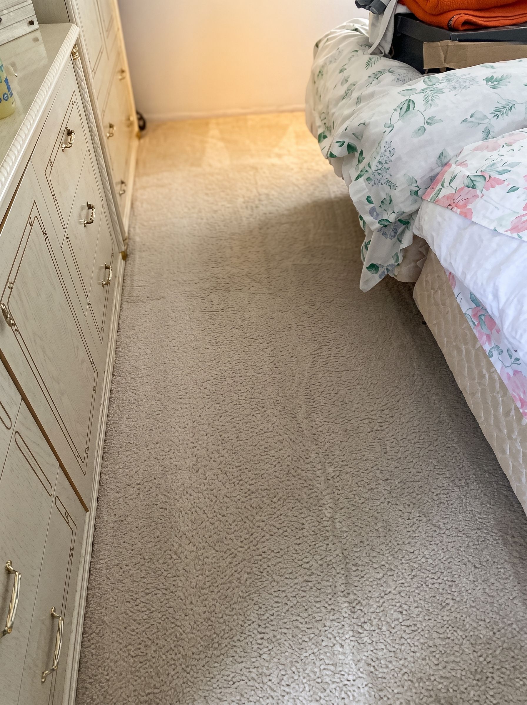 Bedroom with a carpeted floor, white dresser on the left, and a bed with floral bedding on the right.