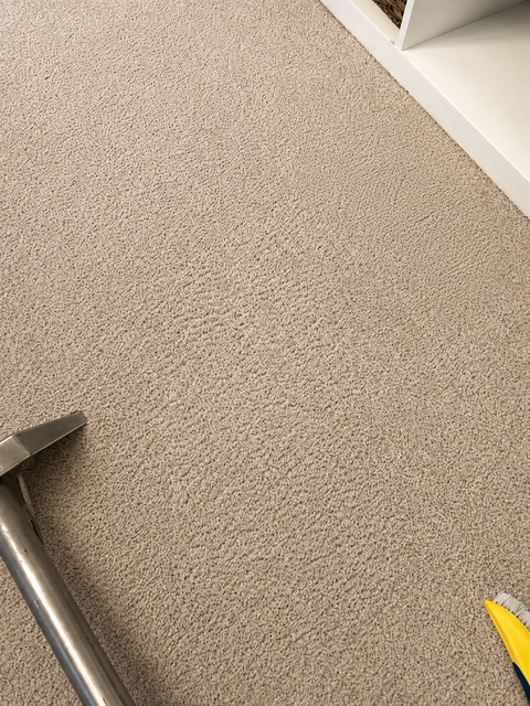 Vacuum cleaner head on beige carpet with a floor nozzle in the lower left corner