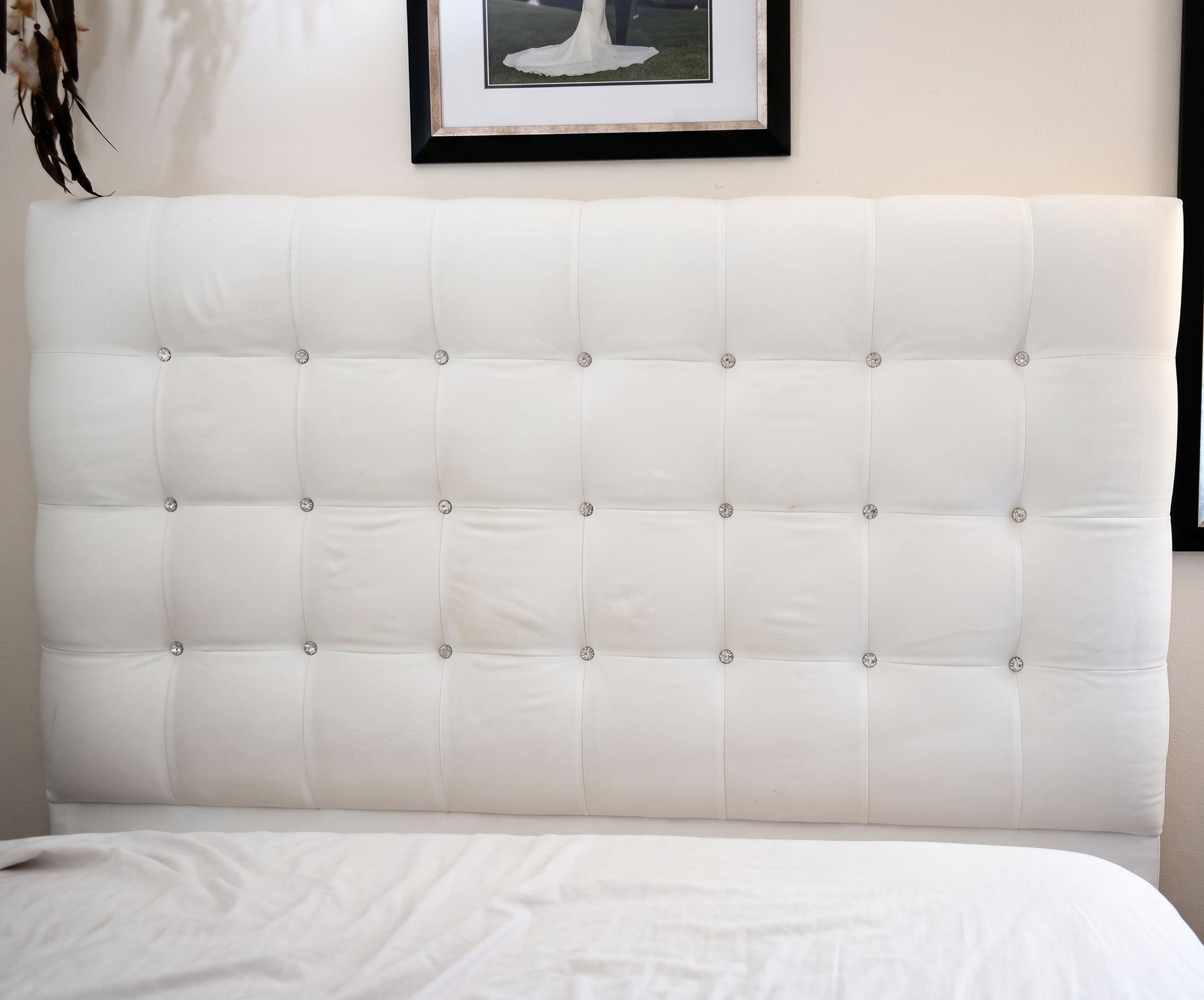 White tufted headboard behind an unmade bed with white sheets and a black-and-white framed print above