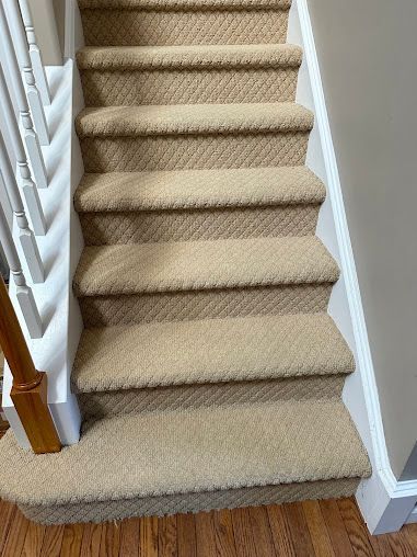 Carpeted indoor staircase with beige runner and white trim, viewed from the bottom.