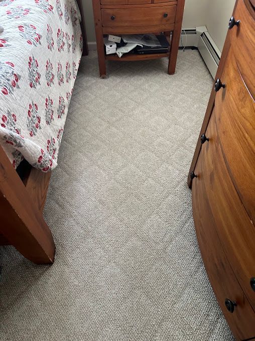 Narrow bedroom aisle between a bed, dresser, and nightstand on beige carpet.