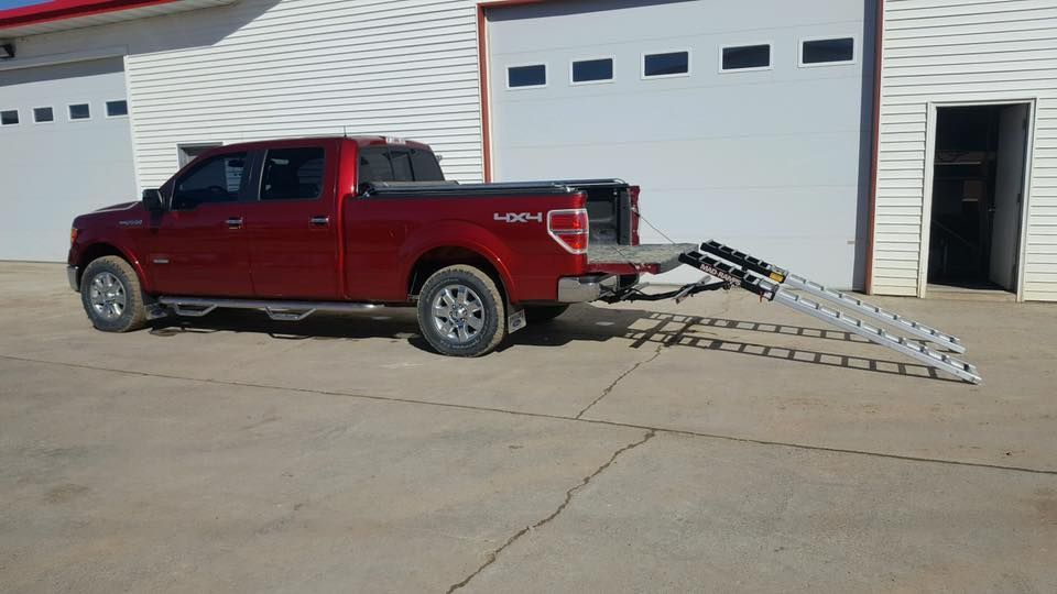 A red truck with a ramp attached to the back is parked in front of a garage.