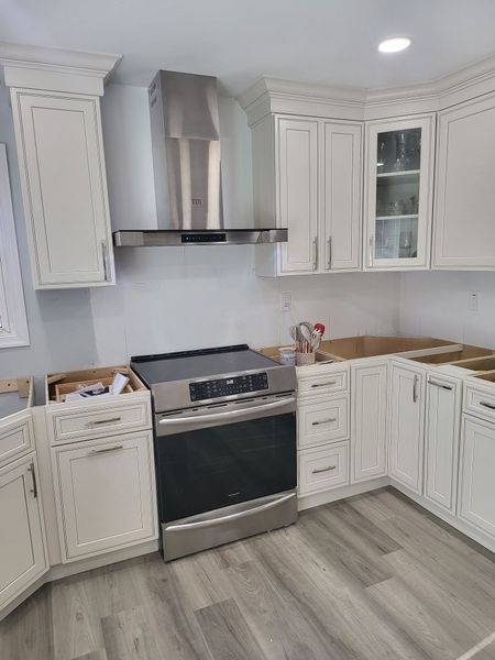 Kitchen with white cabinets, stainless steel range and range hood, unfinished countertops, and wood-look flooring.
