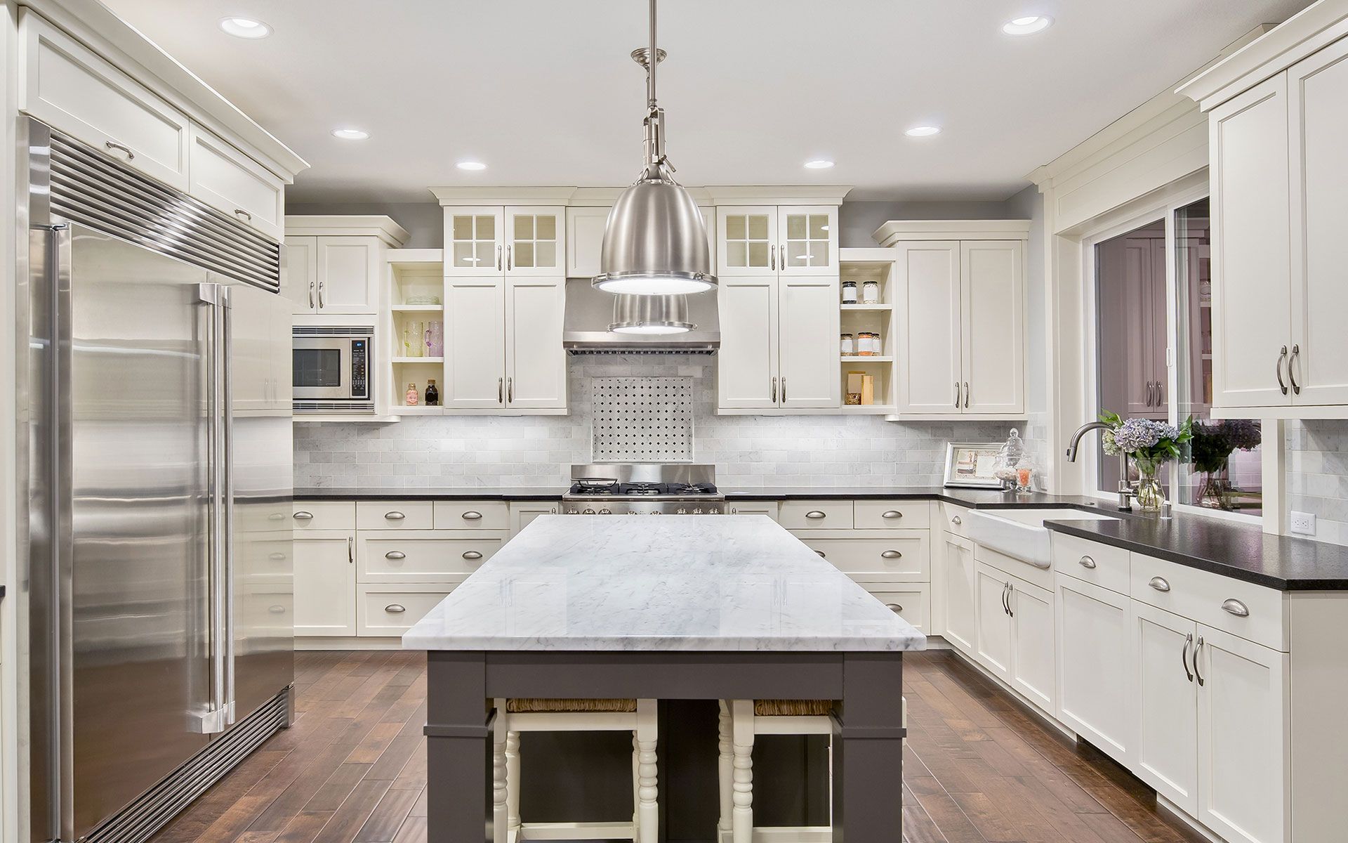 Elegant, bright kitchen with white cabinets, dark countertops, and a central island with a stovetop.