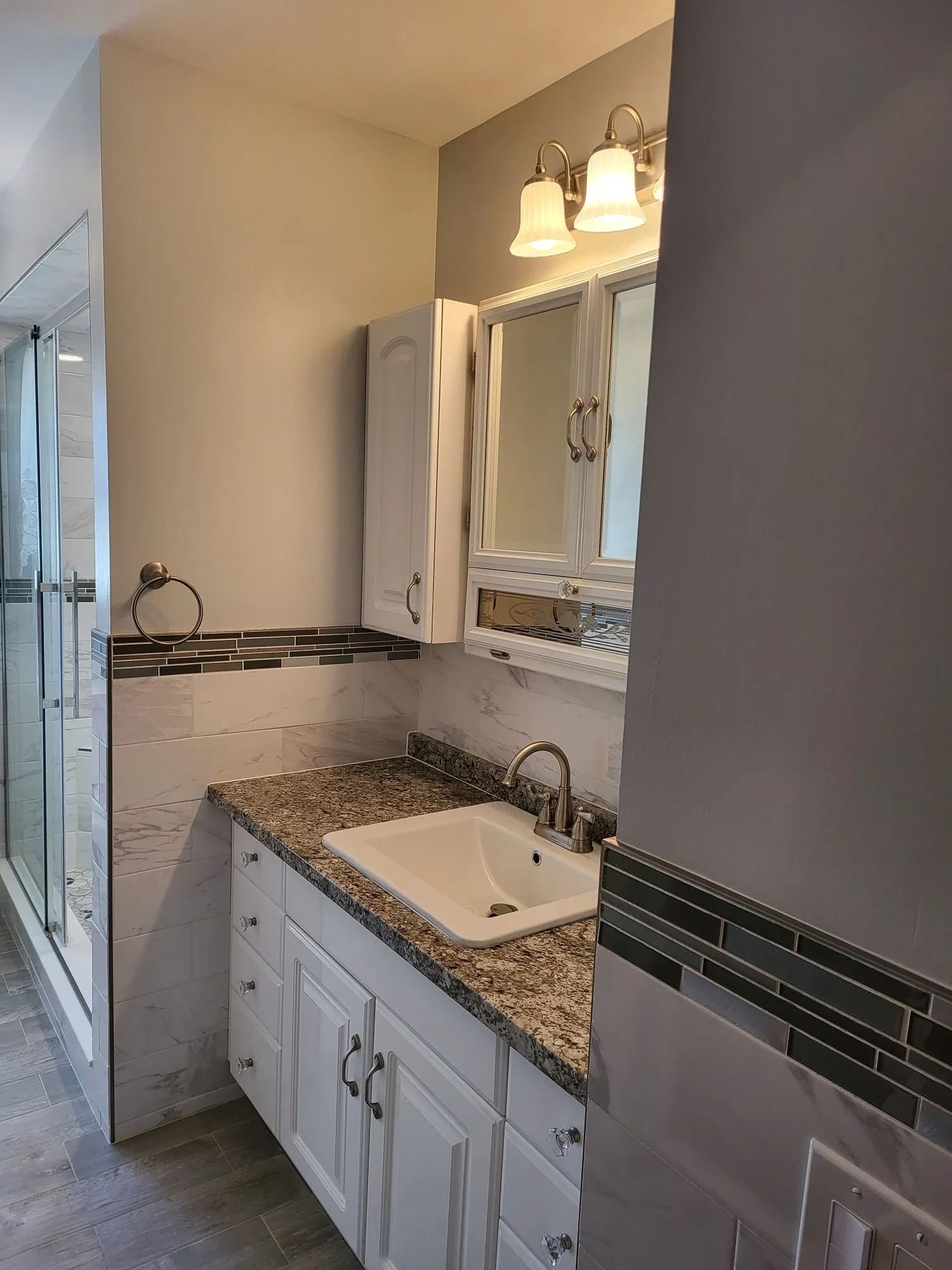 Bathroom with white cabinets, granite countertop, sink, and shower stall.