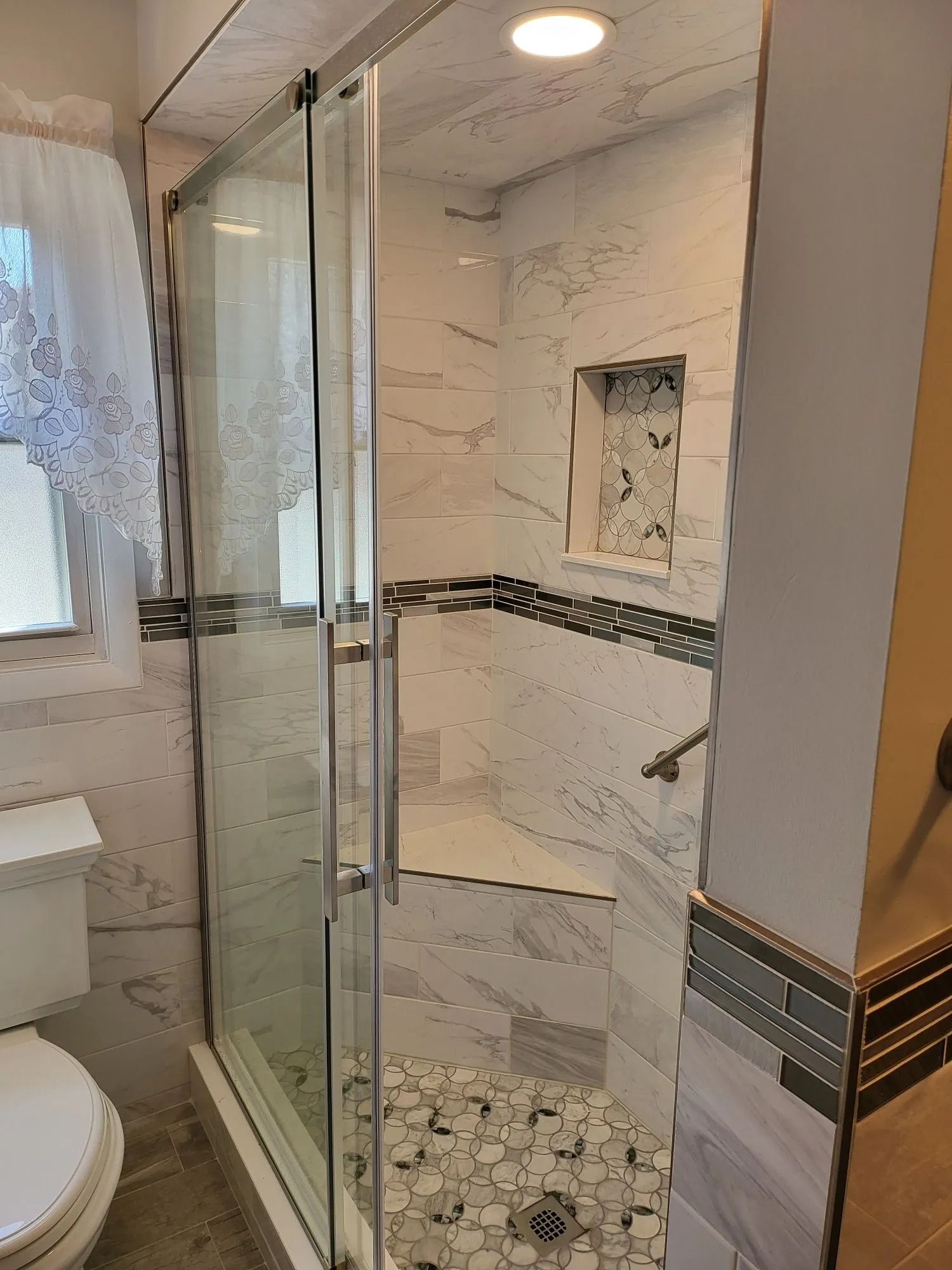 A newly renovated shower with glass door and marble tile. Includes a built-in seat and storage niche.