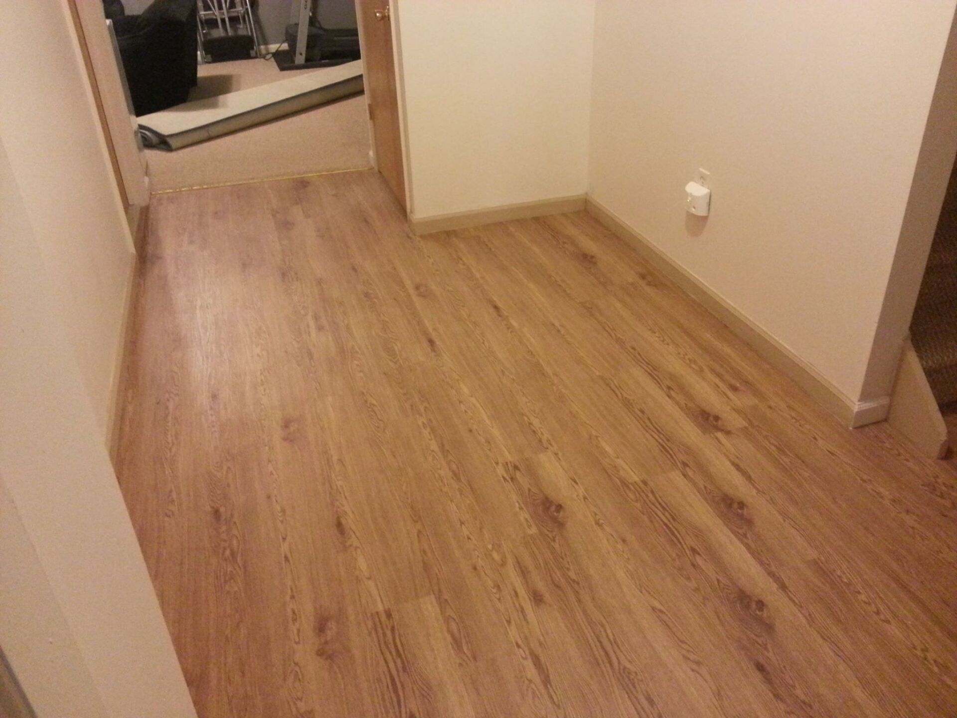 A hallway with light wood-look laminate flooring and beige walls.