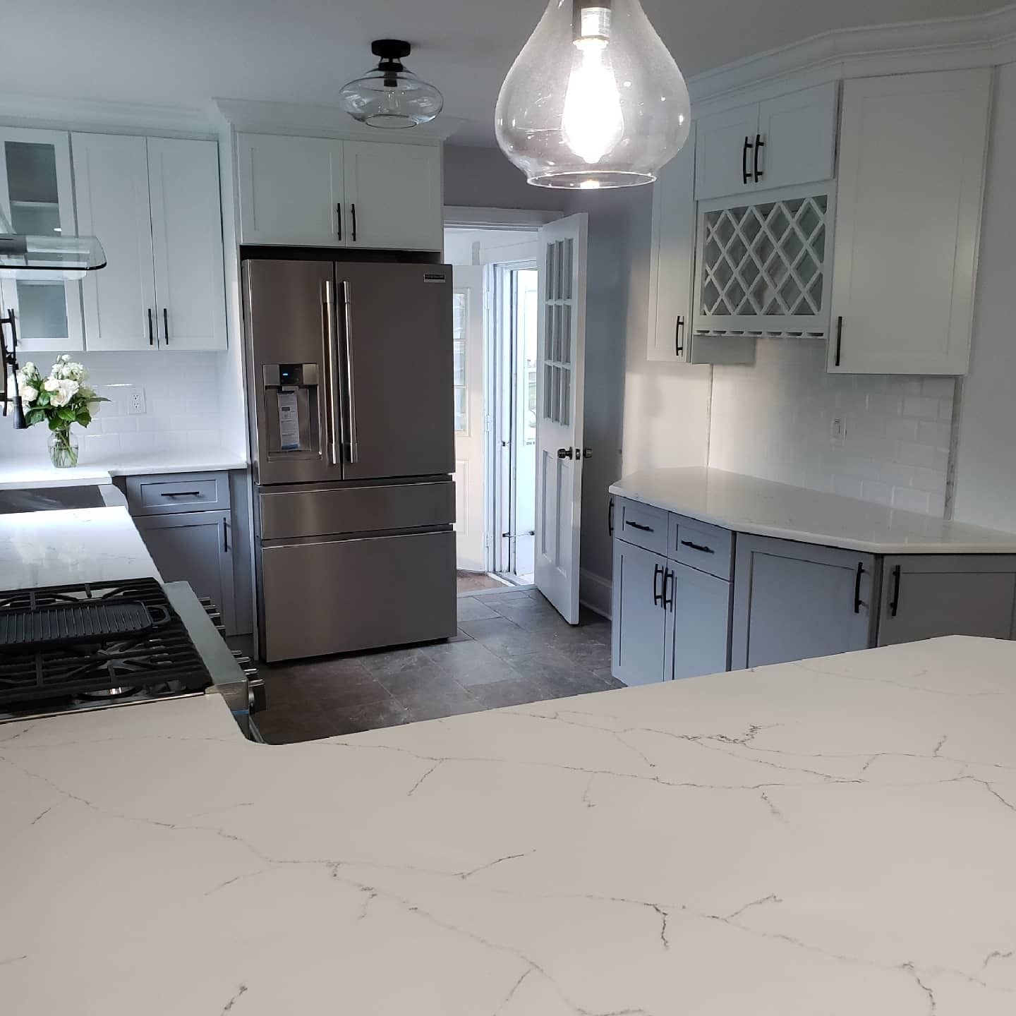 Modern kitchen with white cabinets, stainless steel refrigerator, and large island with marble countertops.