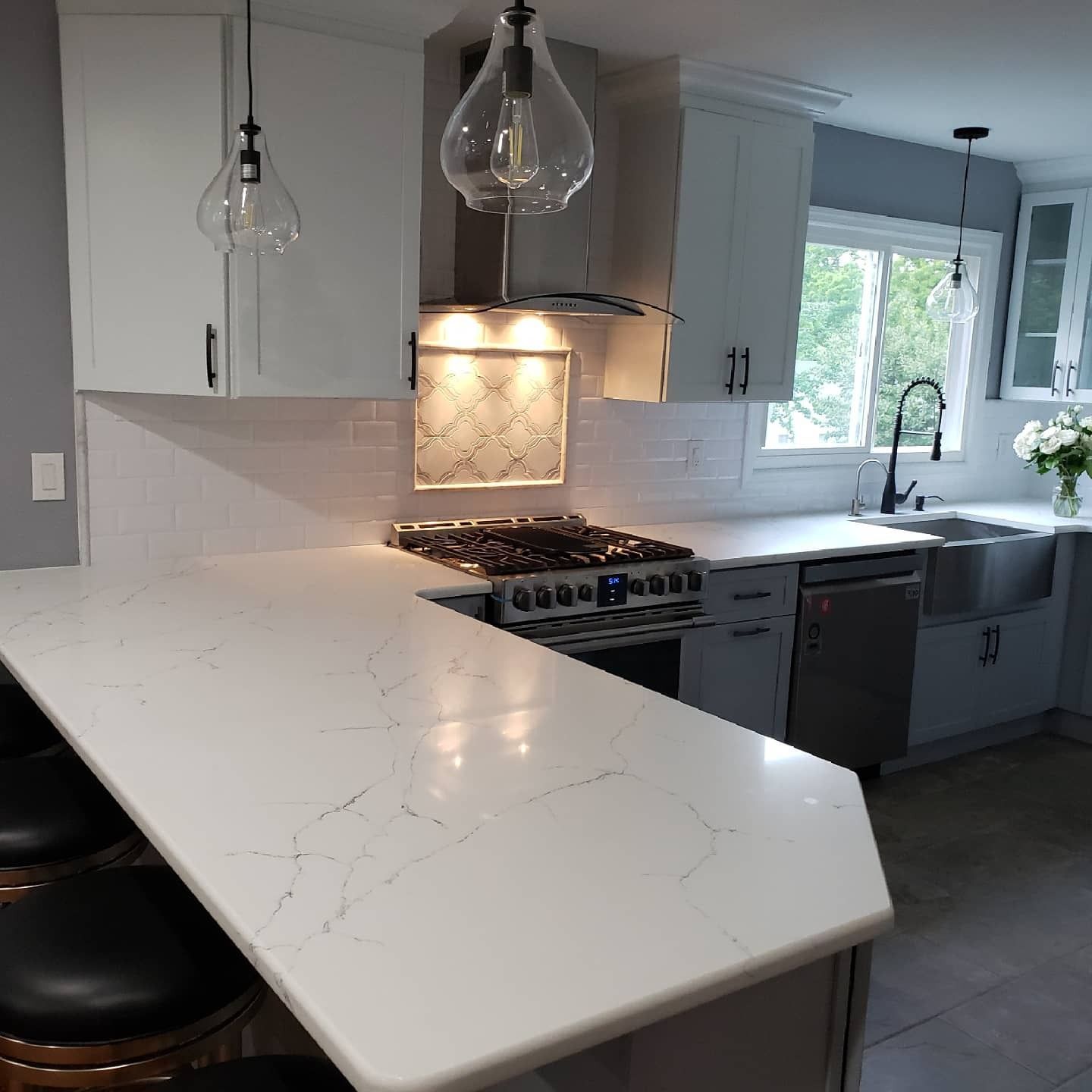 Modern kitchen with white countertops, gray cabinets, stainless steel appliances, and pendant lighting.