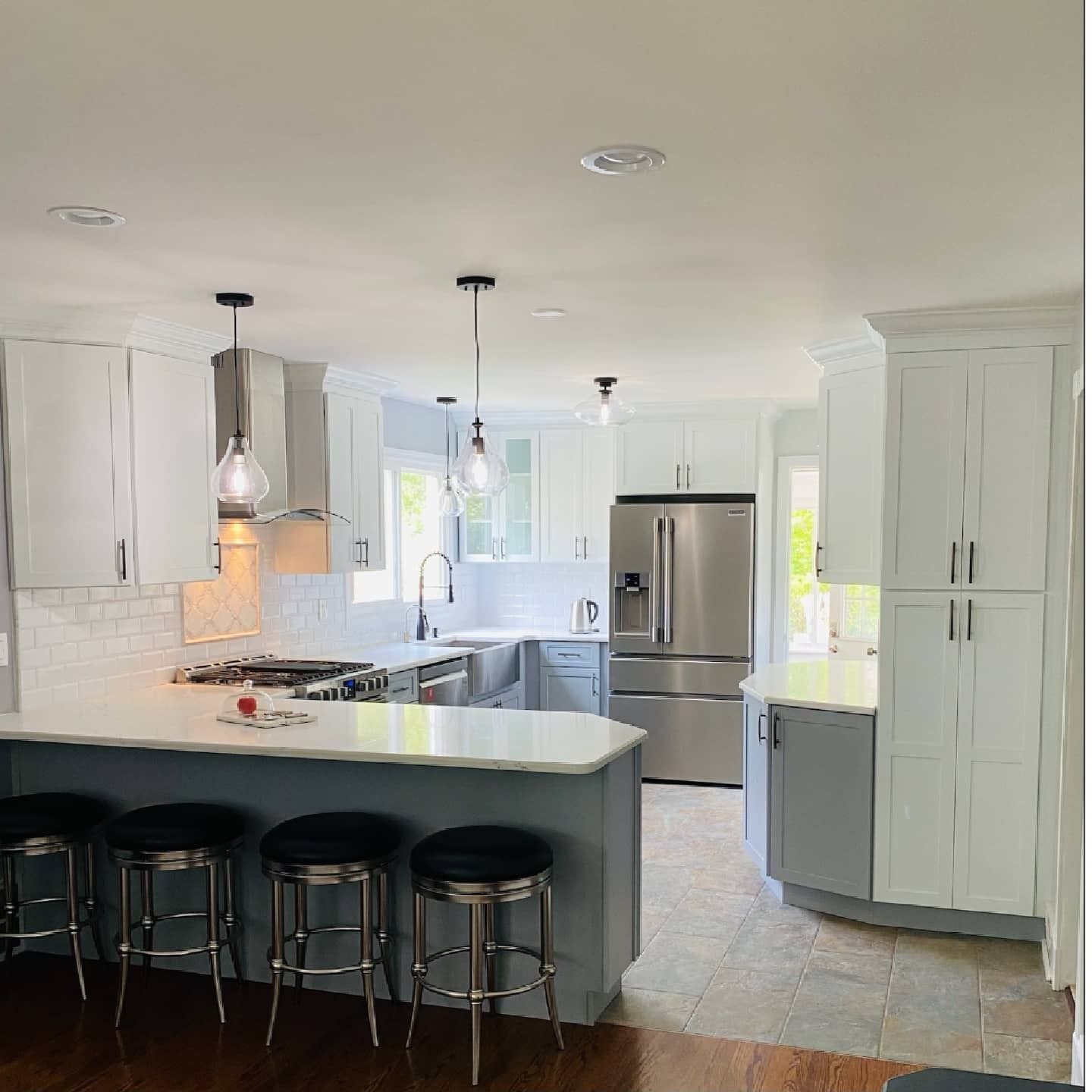 Modern kitchen with white and gray cabinets, stainless steel appliances, and a breakfast bar with stools.