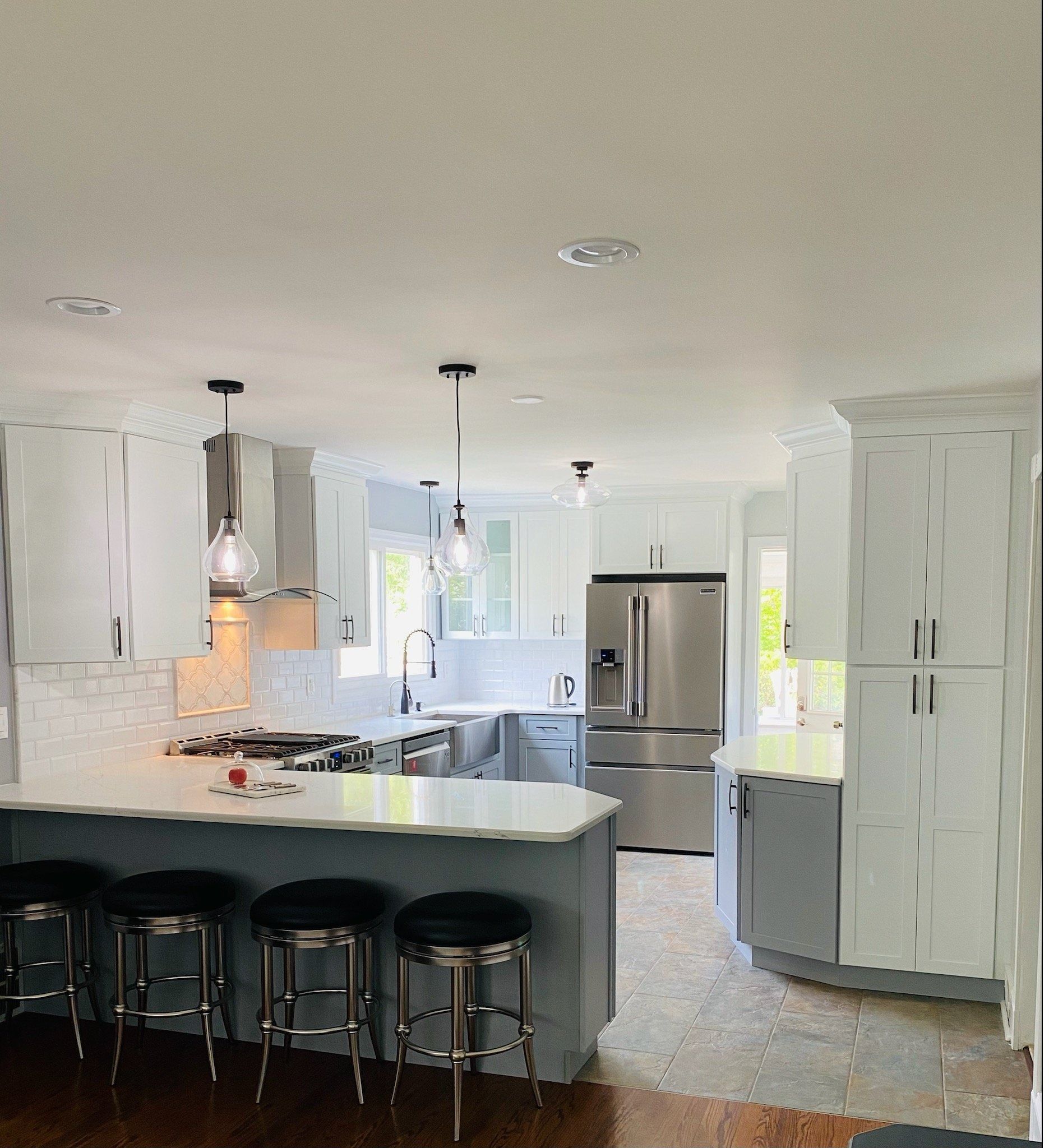 Kitchen with white cabinets, blue island with stools, stainless steel appliances, and pendant lights.