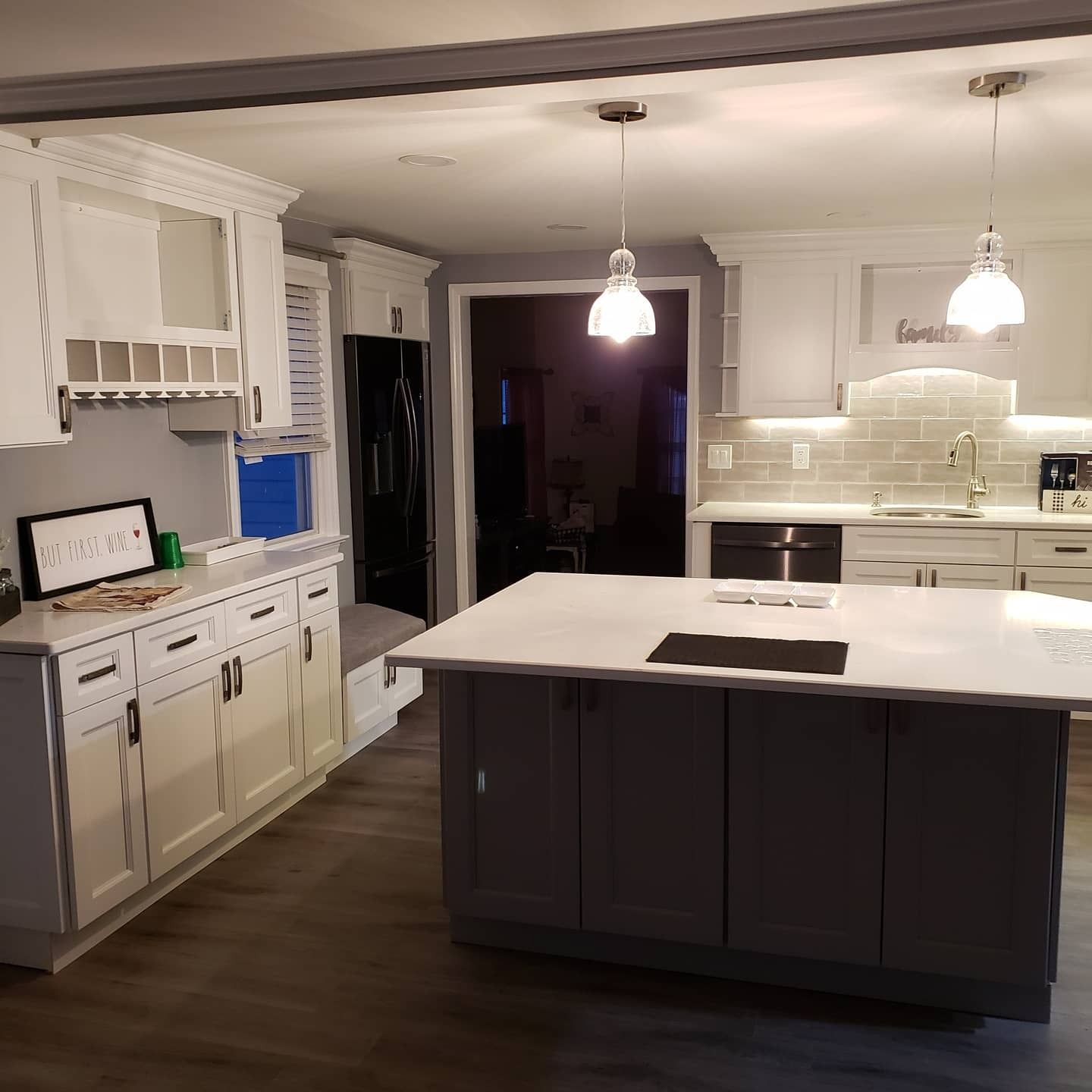 Modern kitchen with white cabinets, gray island, and pendant lights.