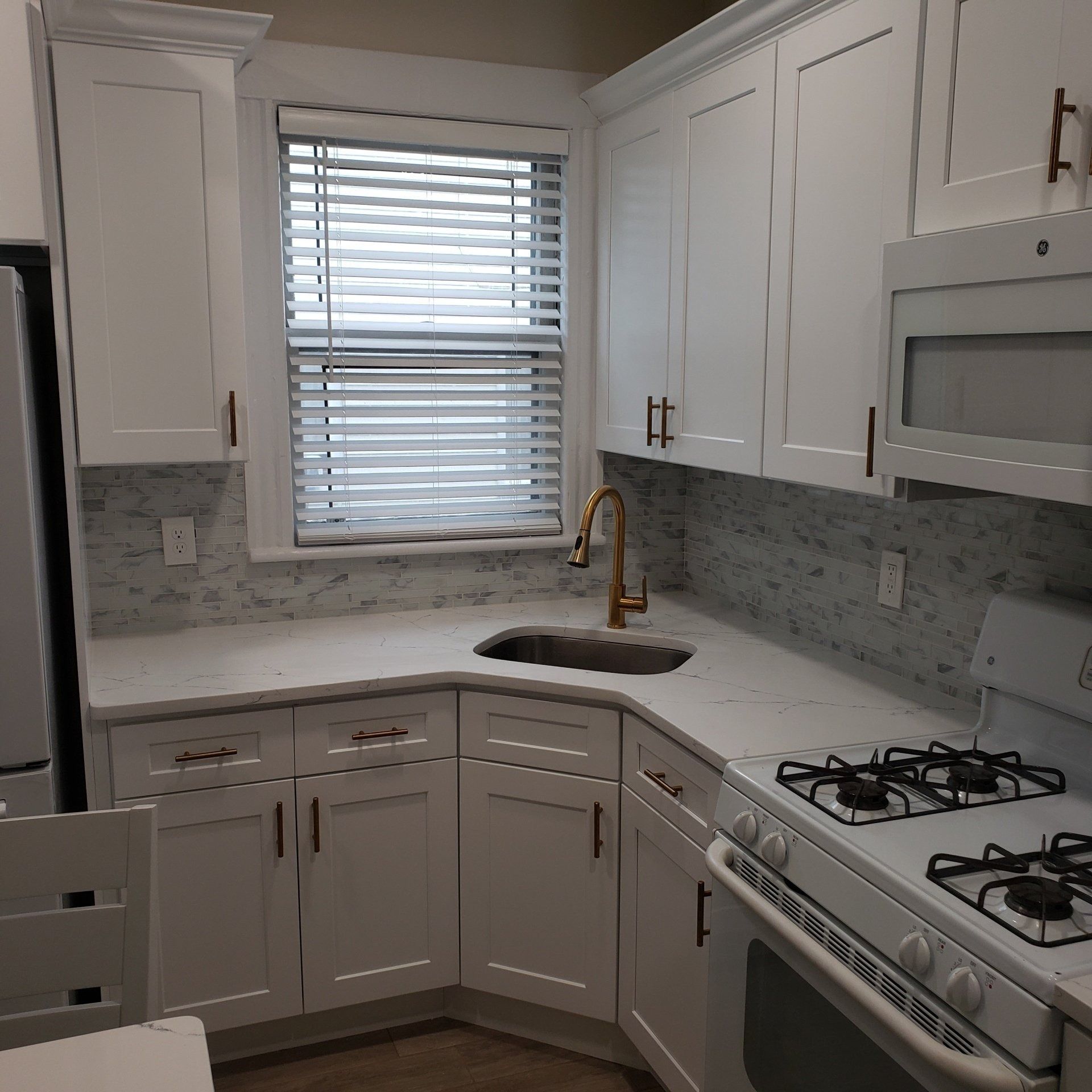 White kitchen cabinets, countertop, and appliances with a window above the sink.