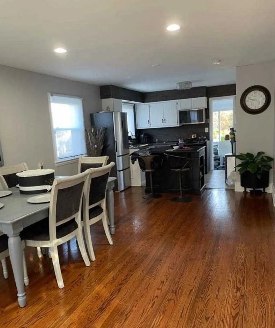 Open-concept kitchen and dining area with dark wood floors, gray walls, white cabinets, and a black island.
