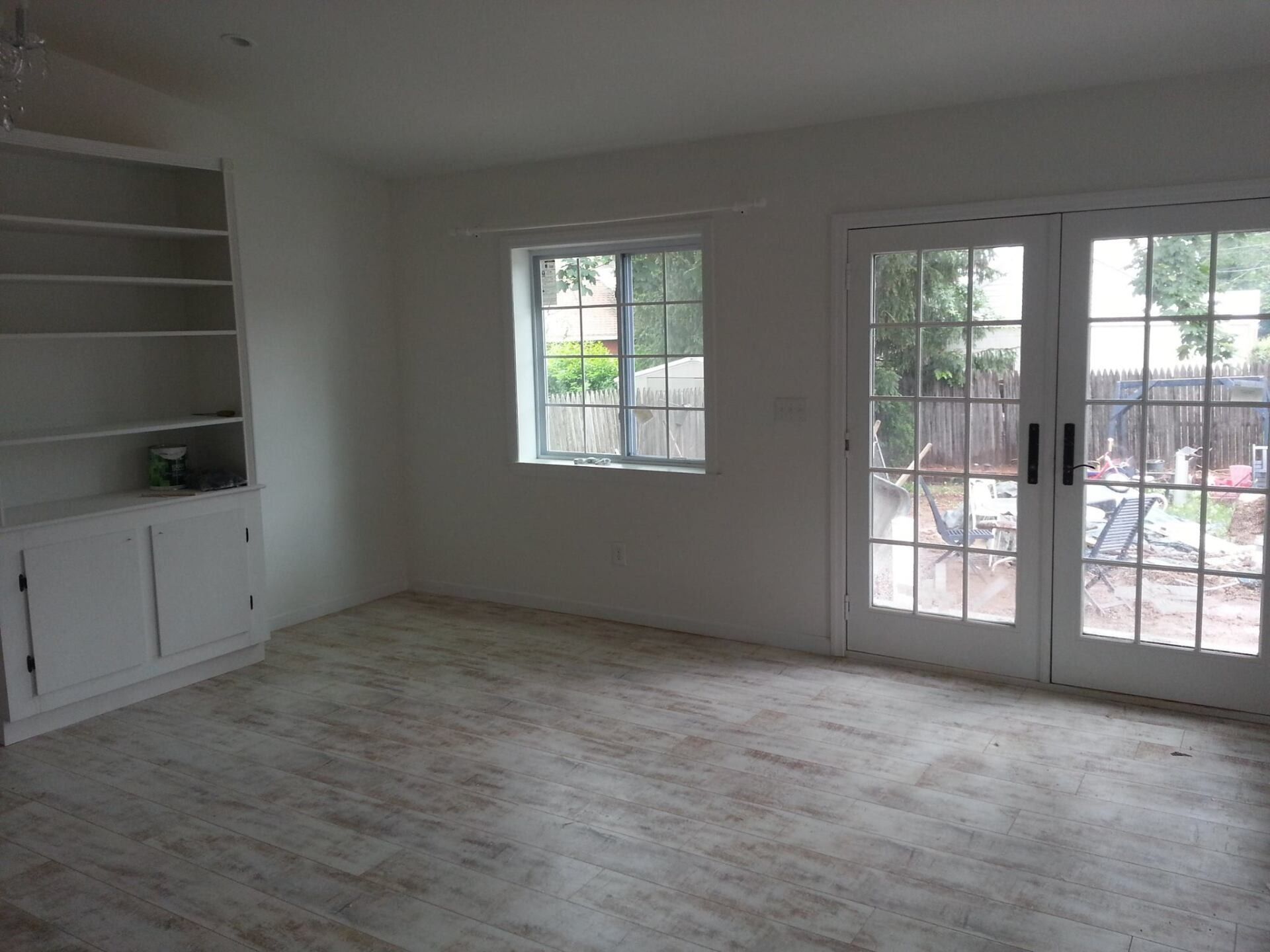 Empty white room with built-in shelves, window, and French doors leading to a backyard.