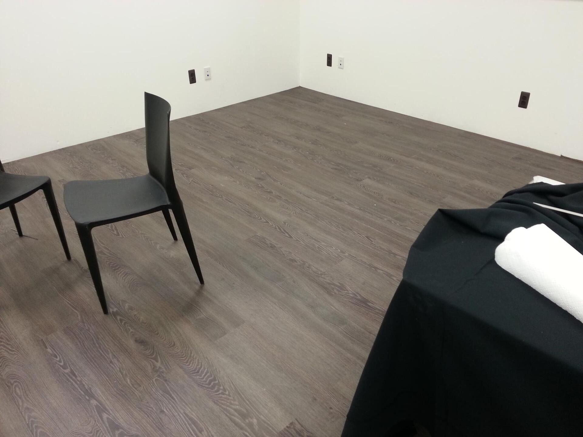 Two black chairs in a corner room with wood-look flooring and white walls. A table covered in black cloth.