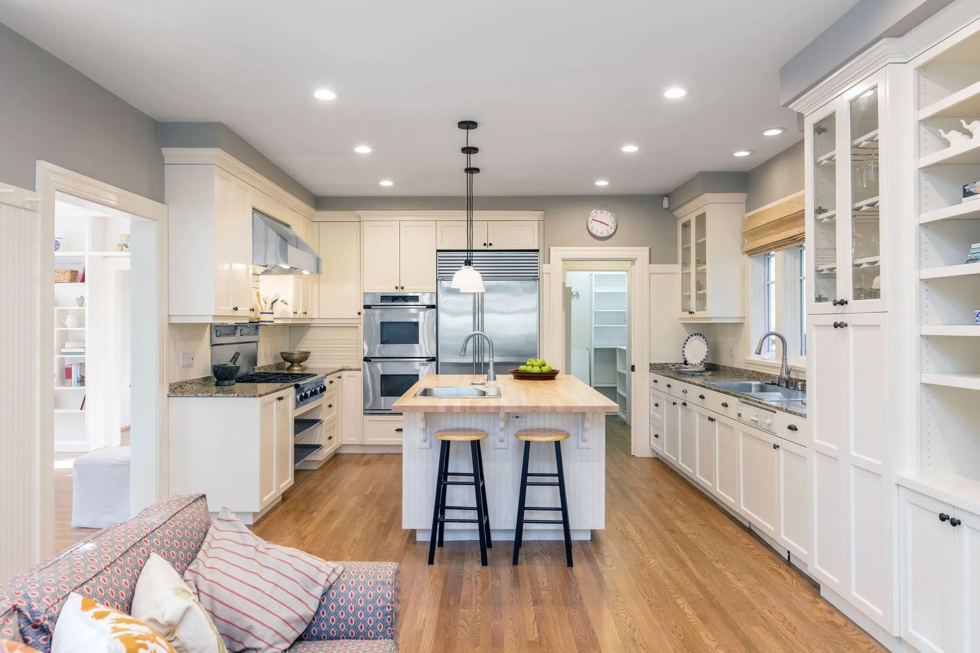 Bright, modern kitchen with white cabinets, wooden floors, stainless steel appliances, and an island with stools.