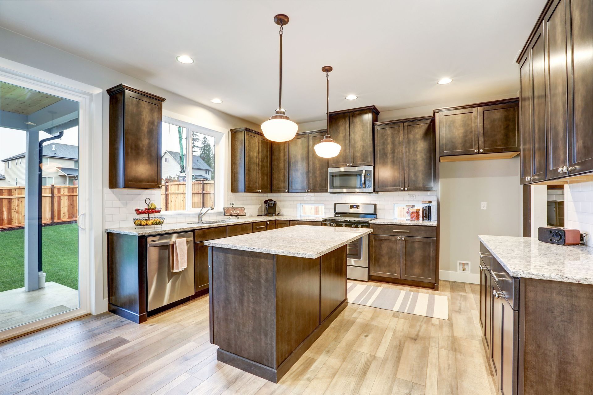 Modern kitchen with dark wood cabinets, island, stainless steel appliances, and white countertops.