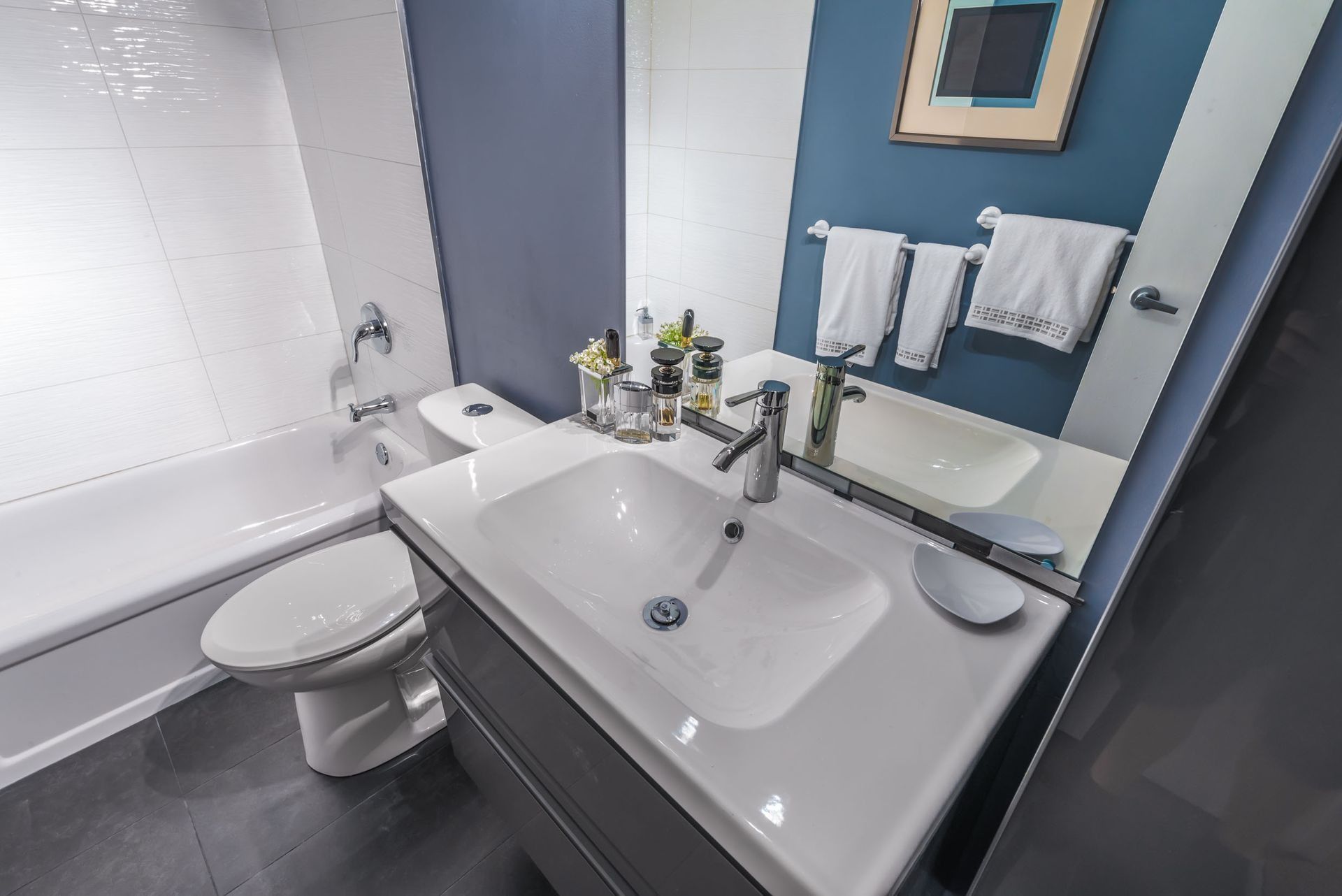 Modern bathroom with a white sink, toilet, bathtub, and blue walls.