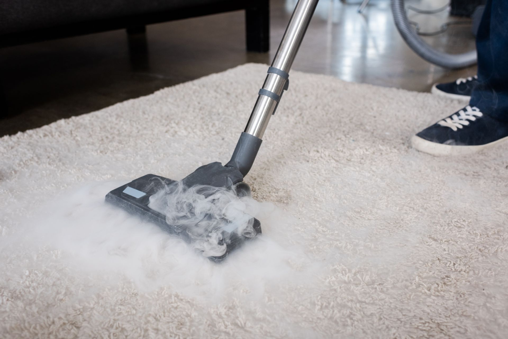 Vacuum cleaner head cleaning a beige carpet, with visible foam or steam around it
