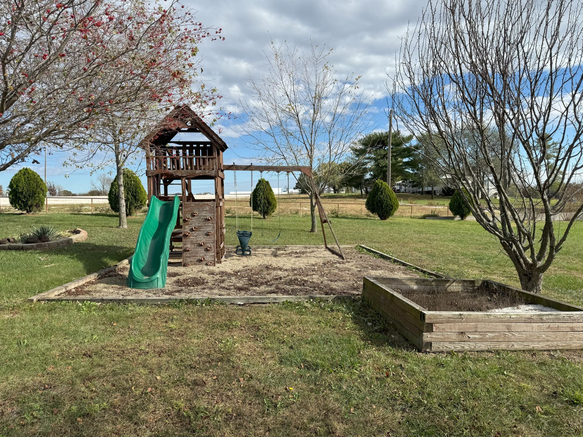A playground with a slide , climbing wall , swings and a sandbox.