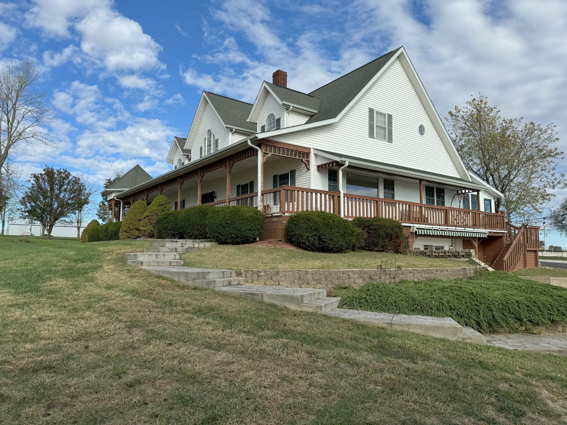 A large white house with a large porch is sitting on top of a grassy hill.