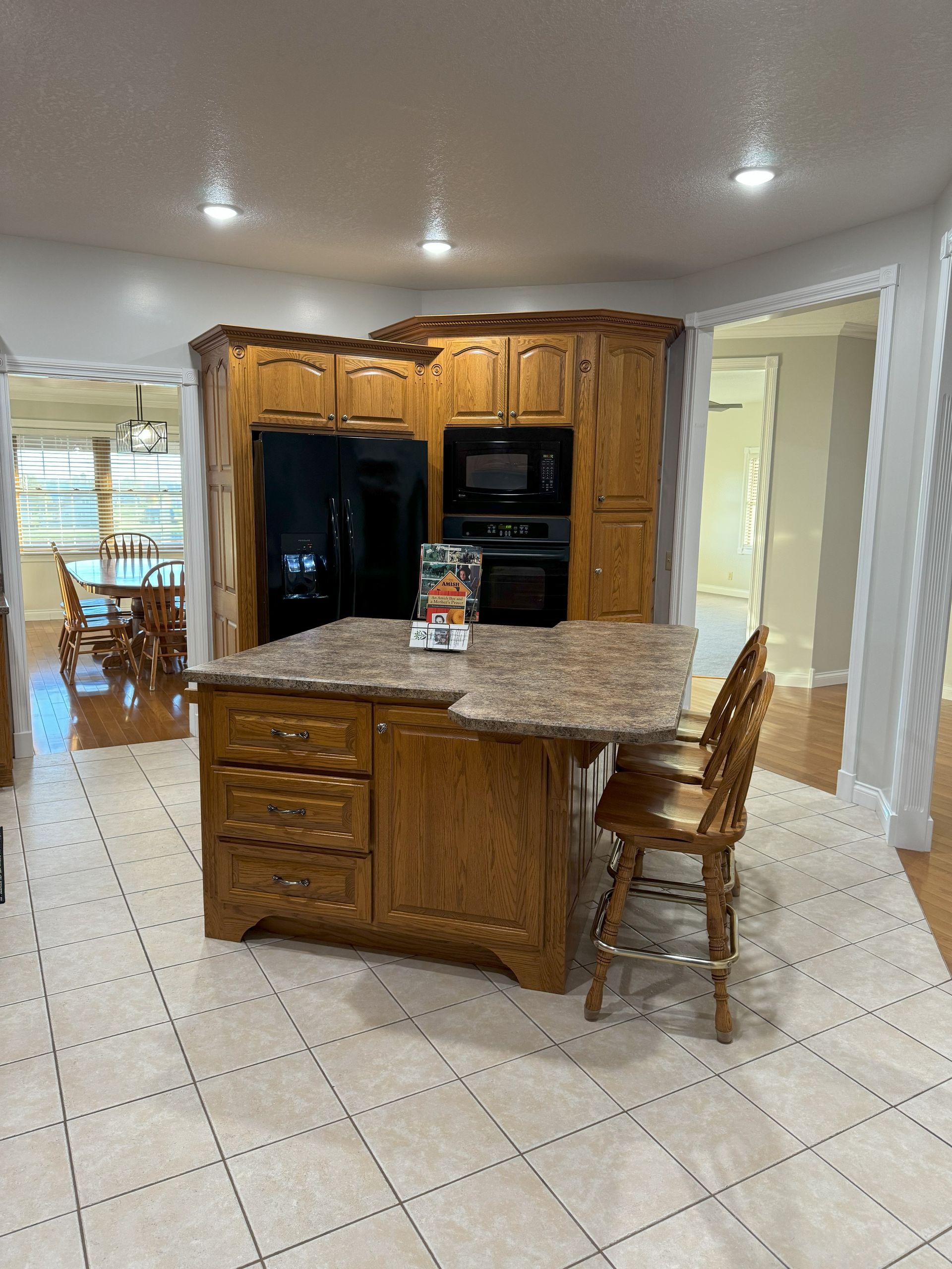 A kitchen with wooden cabinets , granite counter tops , a refrigerator , and a large island.