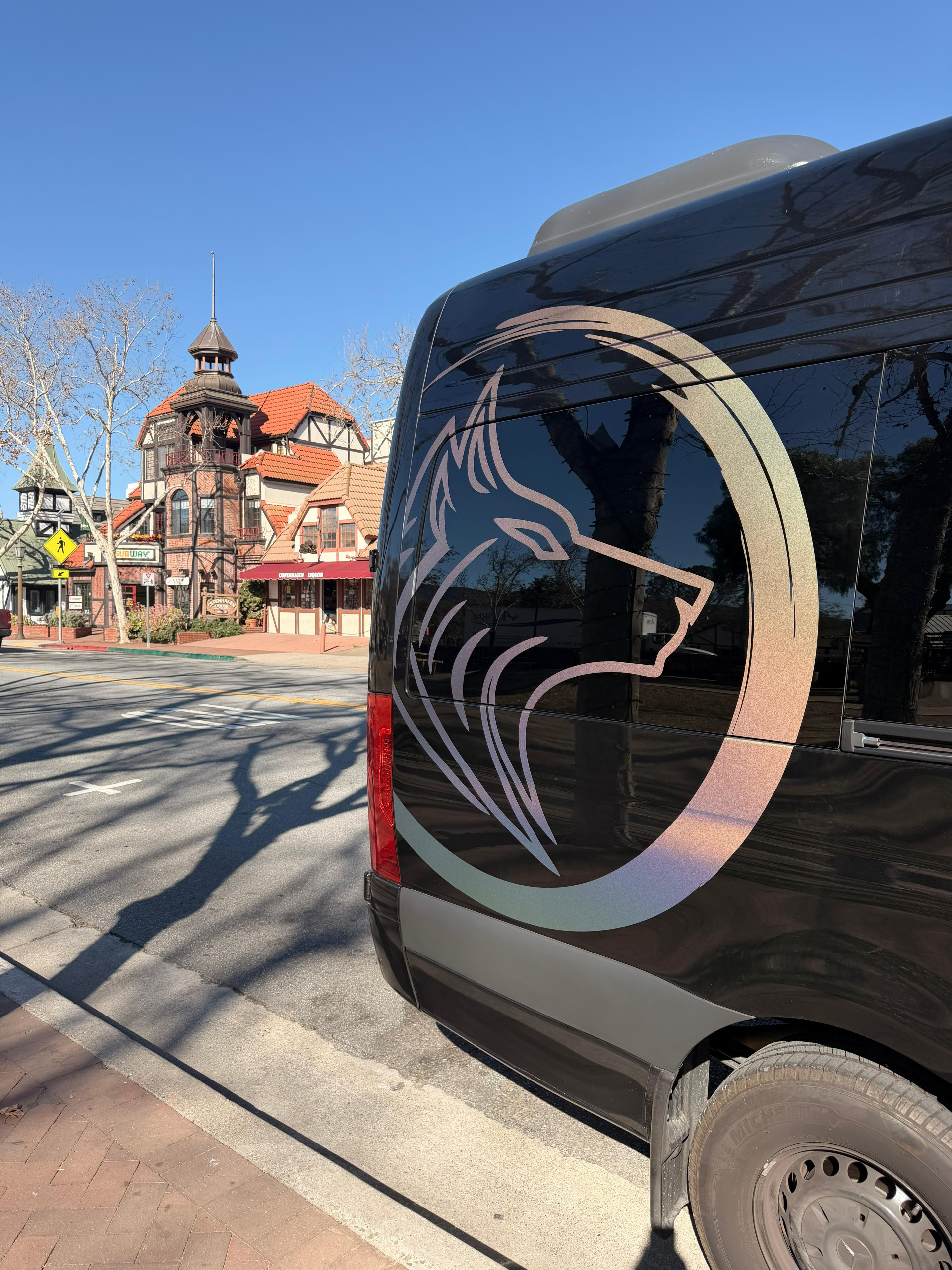 Black van with a wolf logo parked on a sunny street near ornate historic buildings.