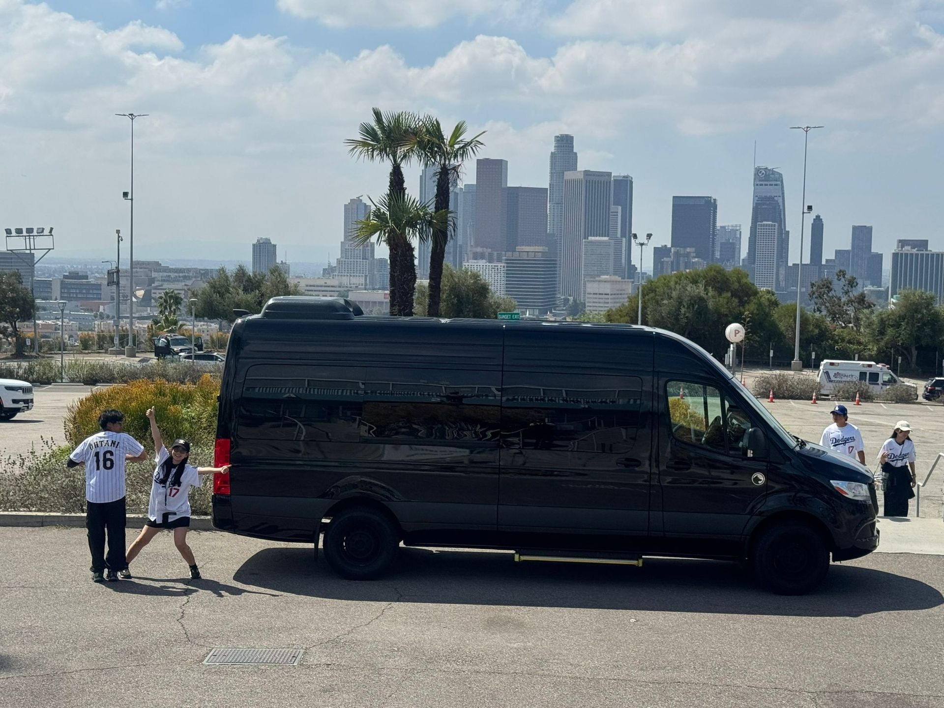 Black van parked by a city overlook with two people standing nearby and skyscrapers in the background