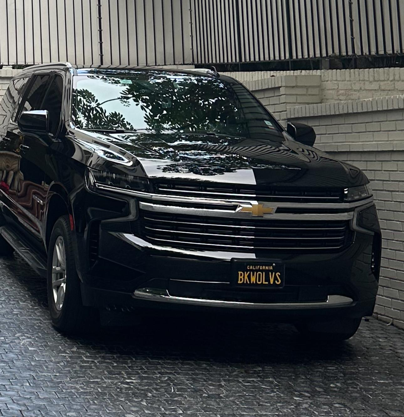 Black Chevrolet SUV parked in a narrow driveway beside a white brick wall